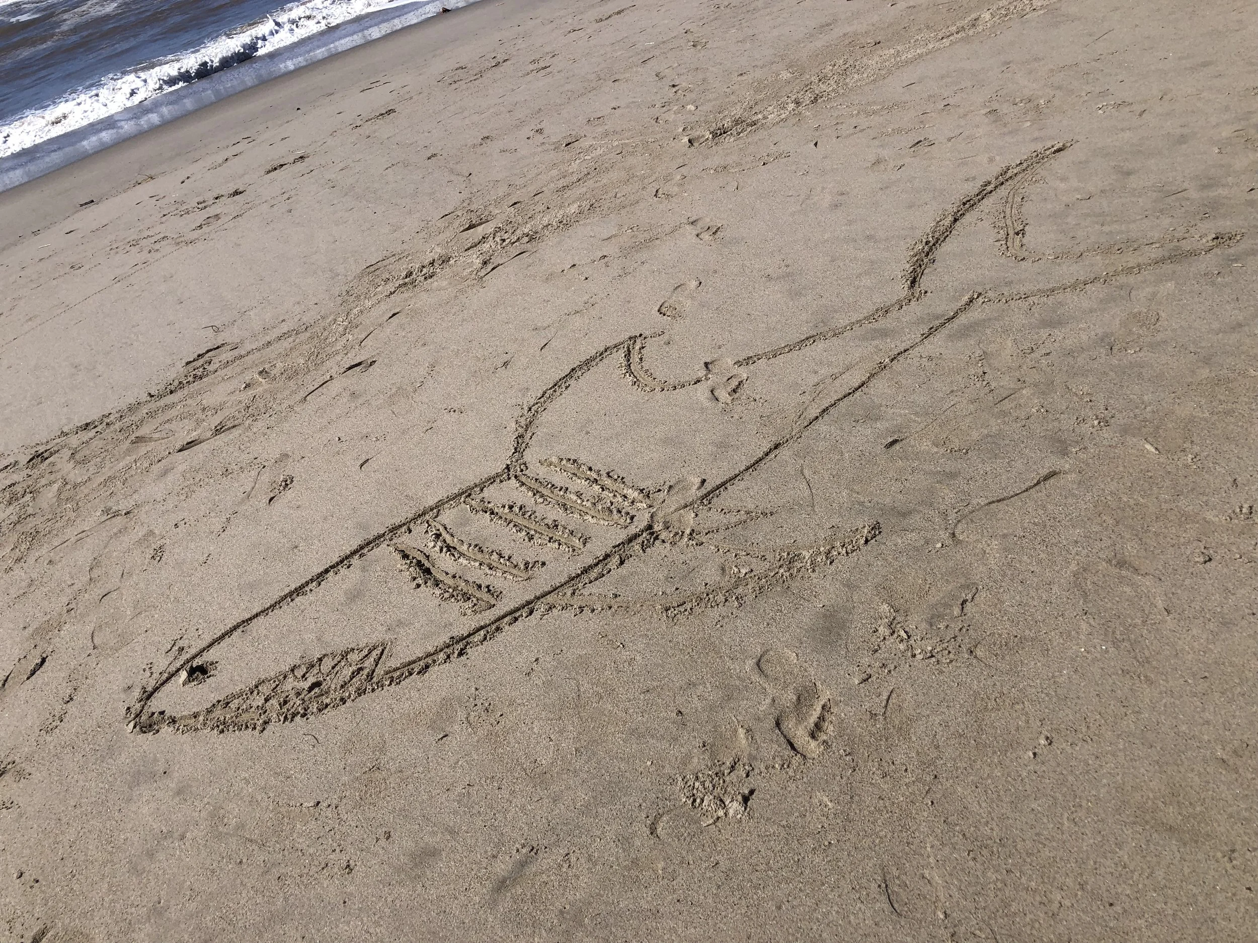 Sand on a beach with the word 'LOVE' written in the sand, near the shoreline with gentle waves.