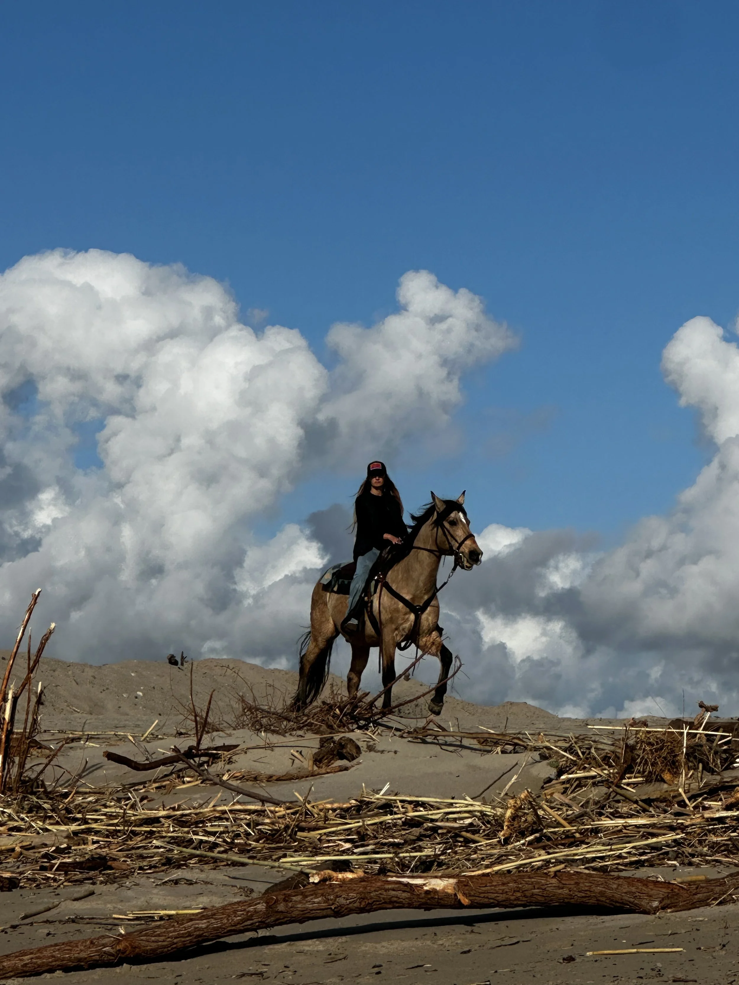 A woman riding a horse on a sandy terrain with a cloudy sky in the background.