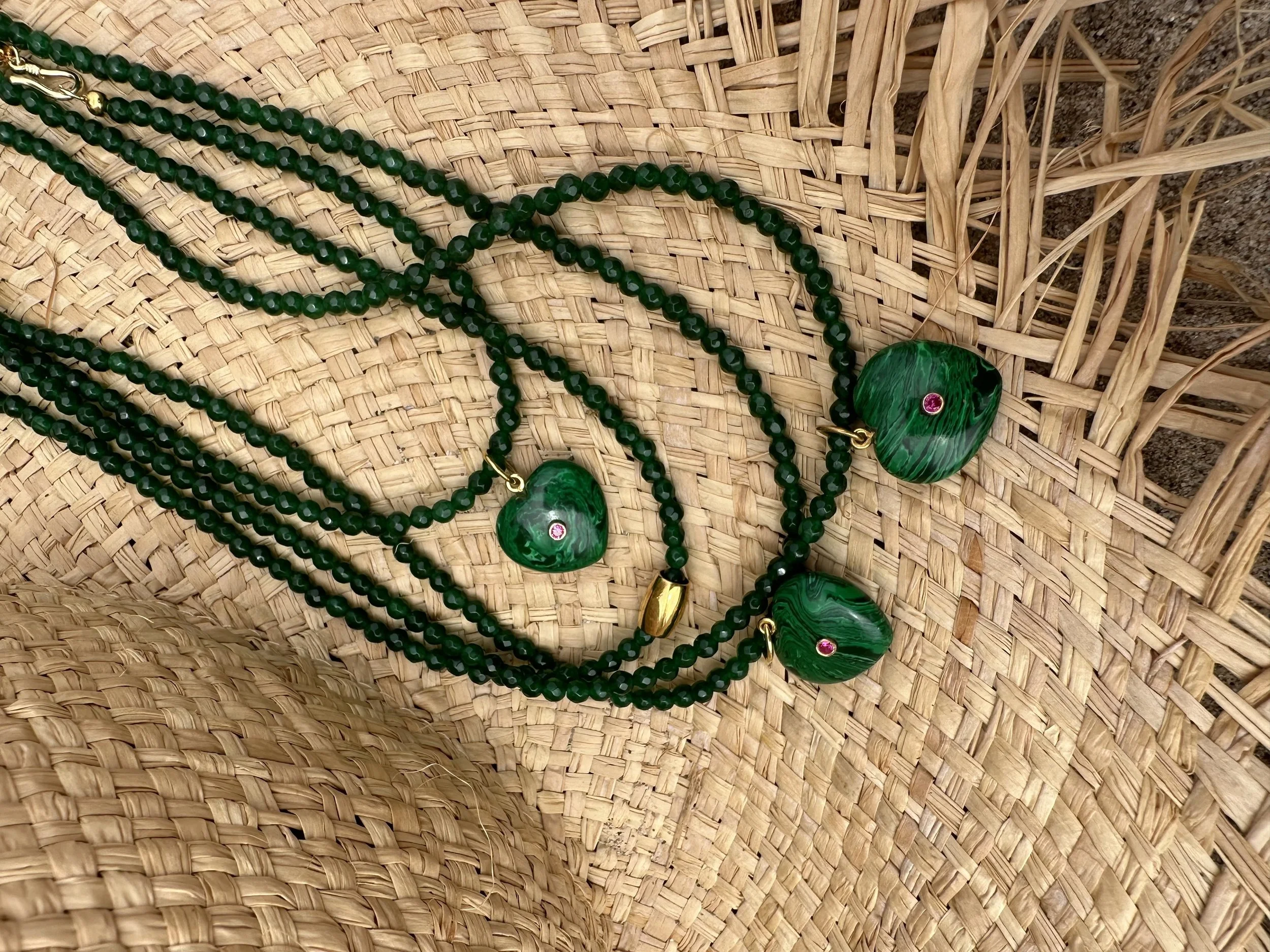 Several strands of green beaded necklaces with large green gemstone pendants on a woven straw surface.