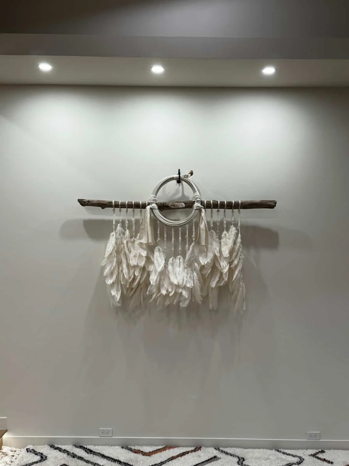 Wall art decor made from a wooden stick, metal rings, and white fabric tassels hanging beneath, mounted on a plain white wall.