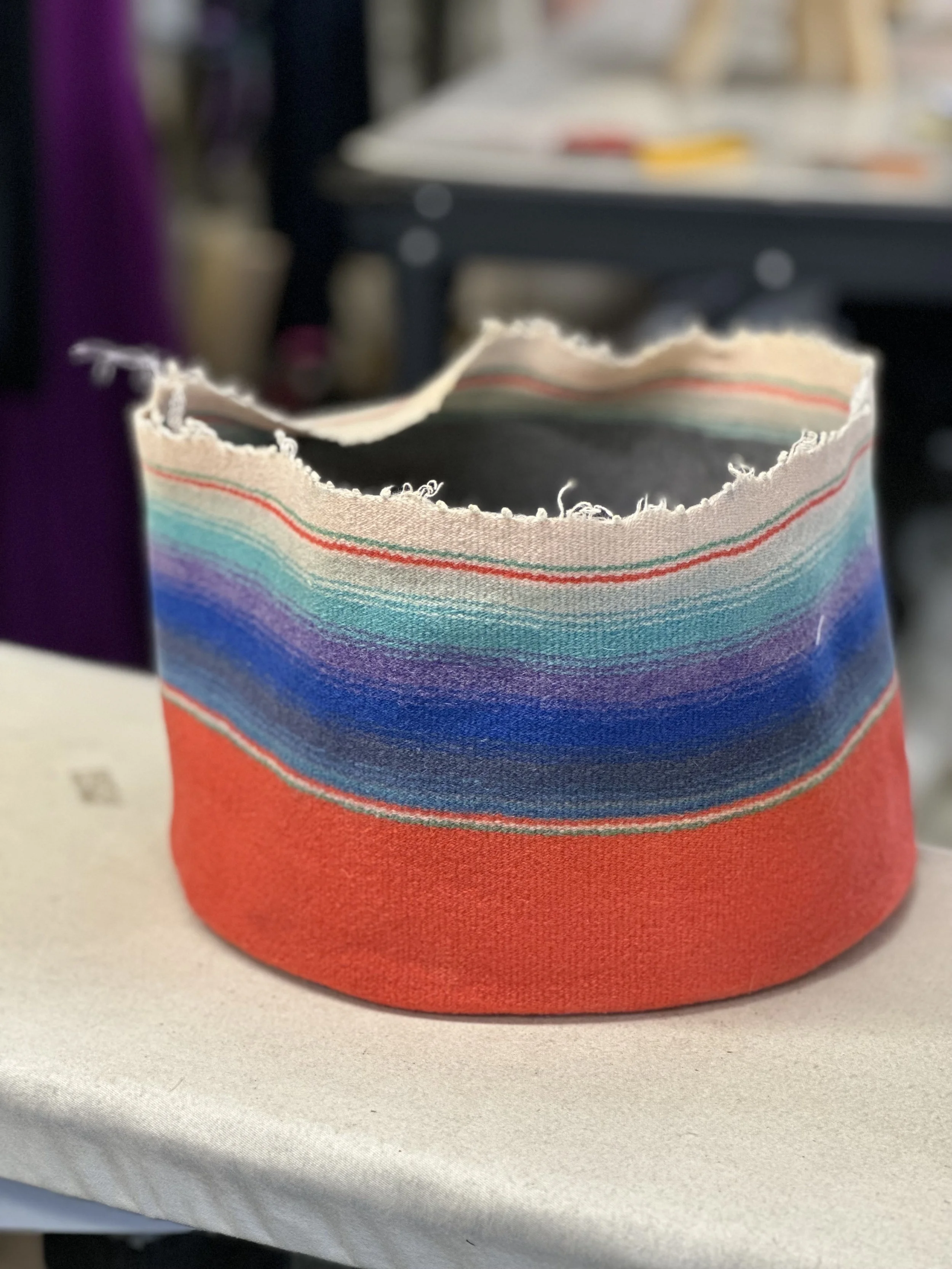A colorful fabric with horizontal rainbow stripes and frayed edges, placed on a white surface.