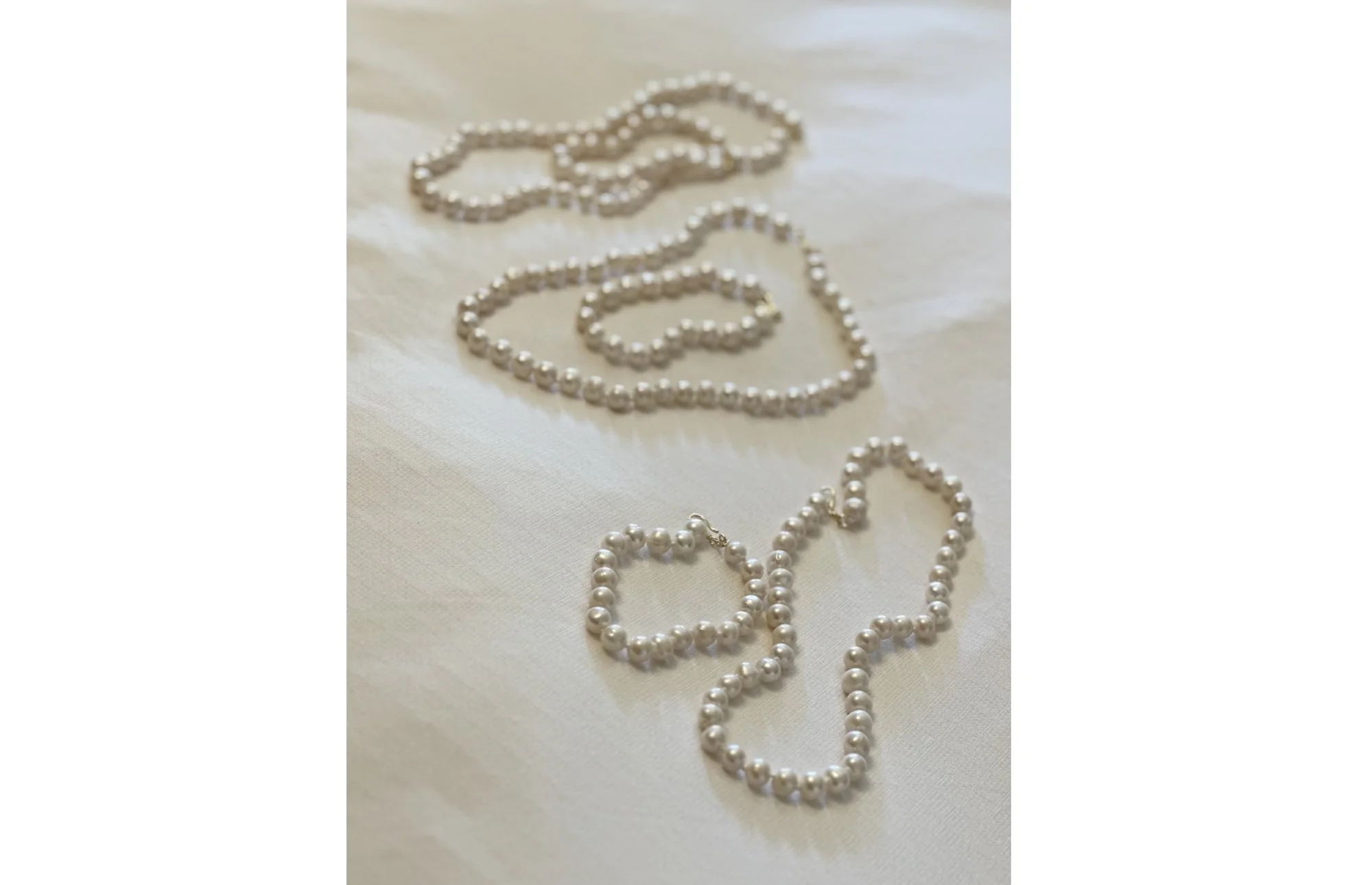 Various pearl necklaces and bracelets laid out on a white fabric surface.