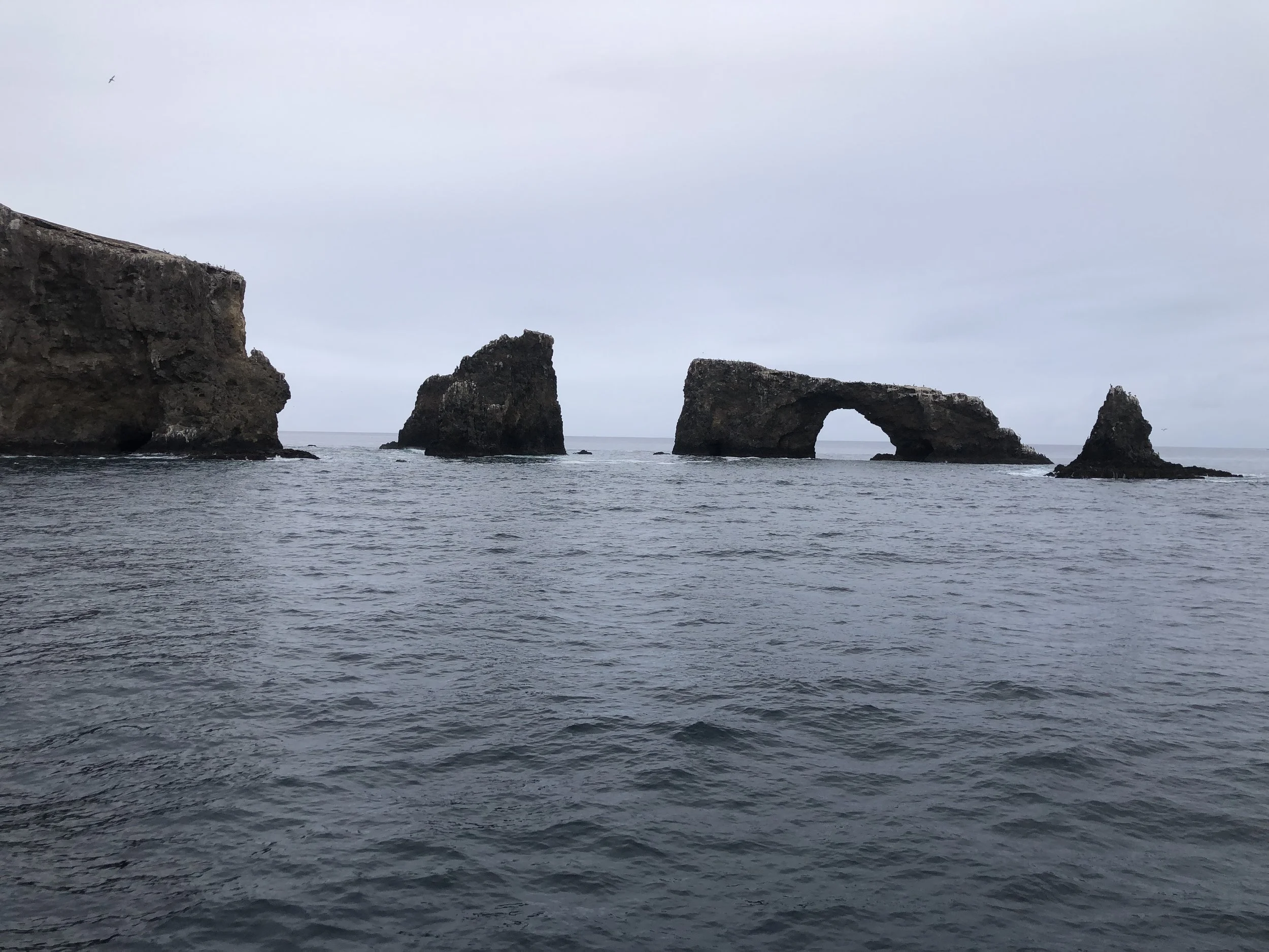 Overcast sky and ocean with large rock formations, including one with a natural arch.