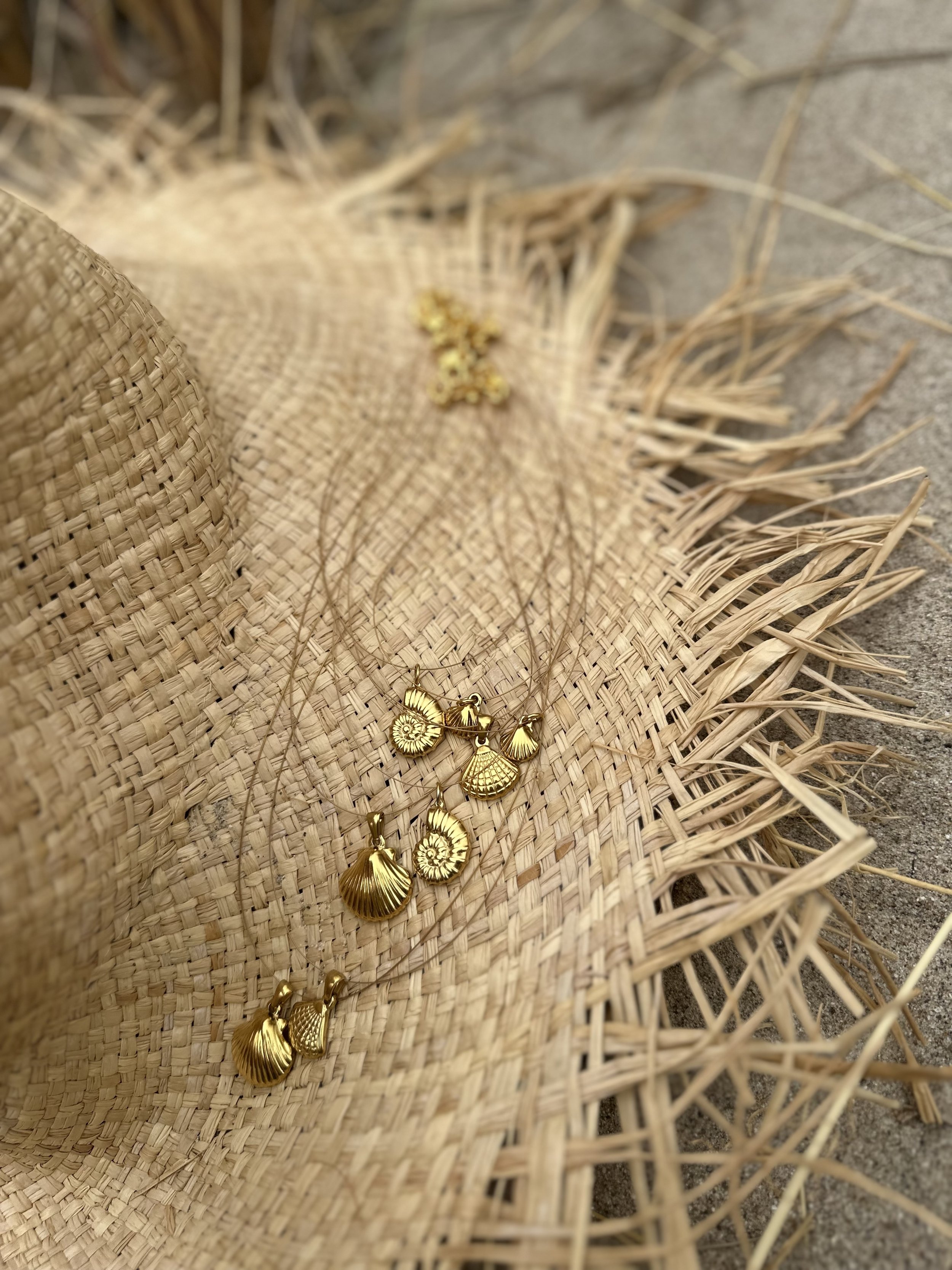 Gold seashell jewelry on a woven straw fan with straw grass and a straw hat nearby.