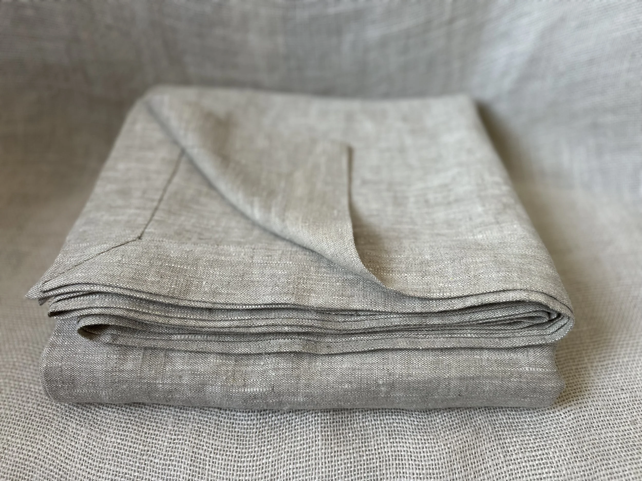 A neatly folded stack of light gray fabric napkins or towels placed on a textured gray surface.