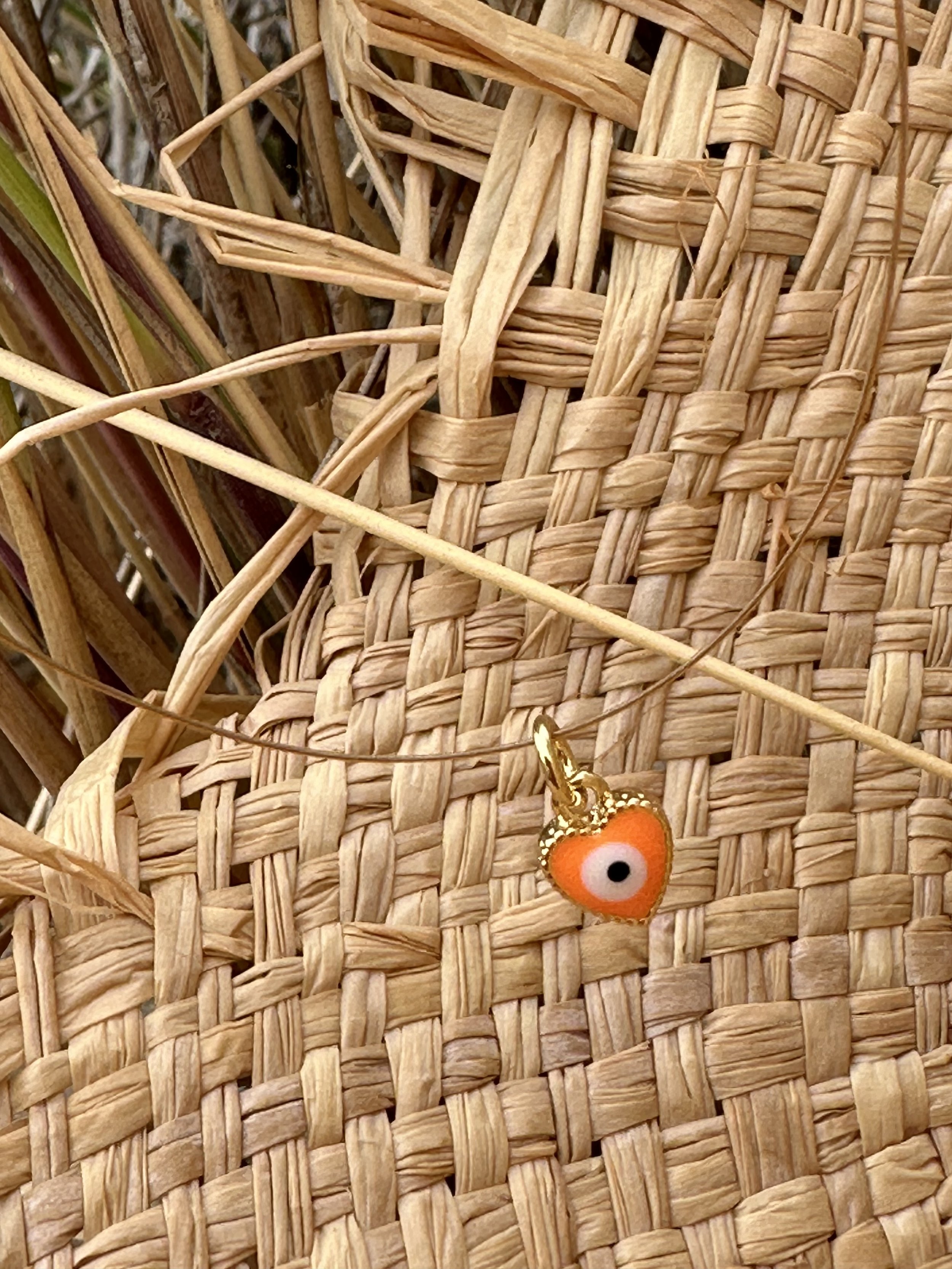 Close-up of woven straw or wicker material with a small decorative orange and white eye charm attached to it.