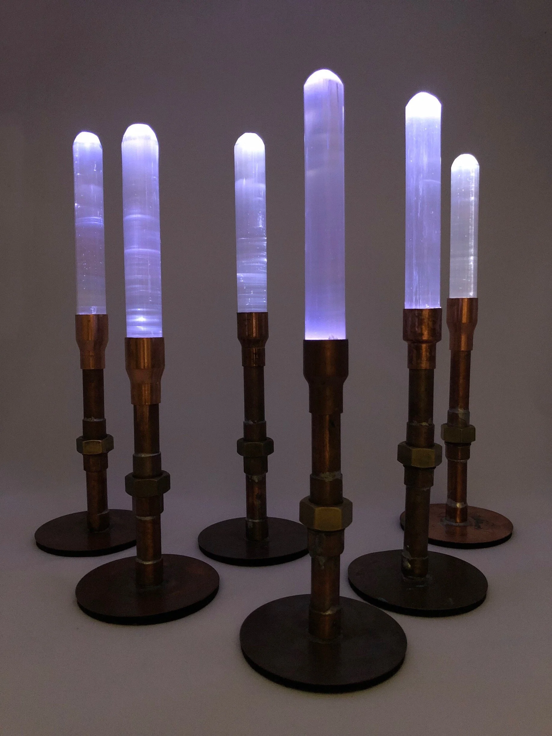 Six illuminated glass tubes mounted on metal stands with round bases, arranged in a row against a dark background.