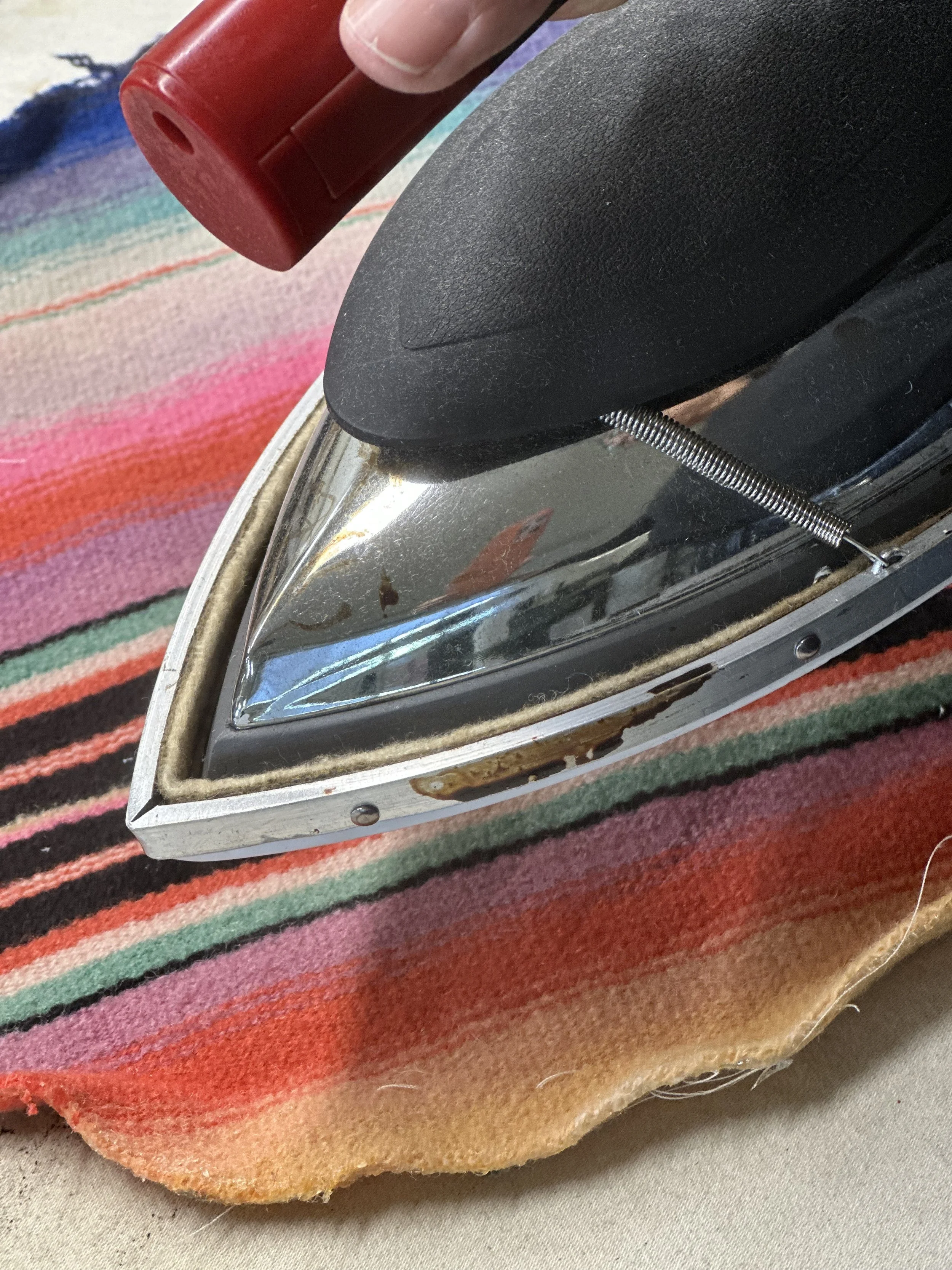 Close-up of an iron resting on a colorful, striped fabric.
