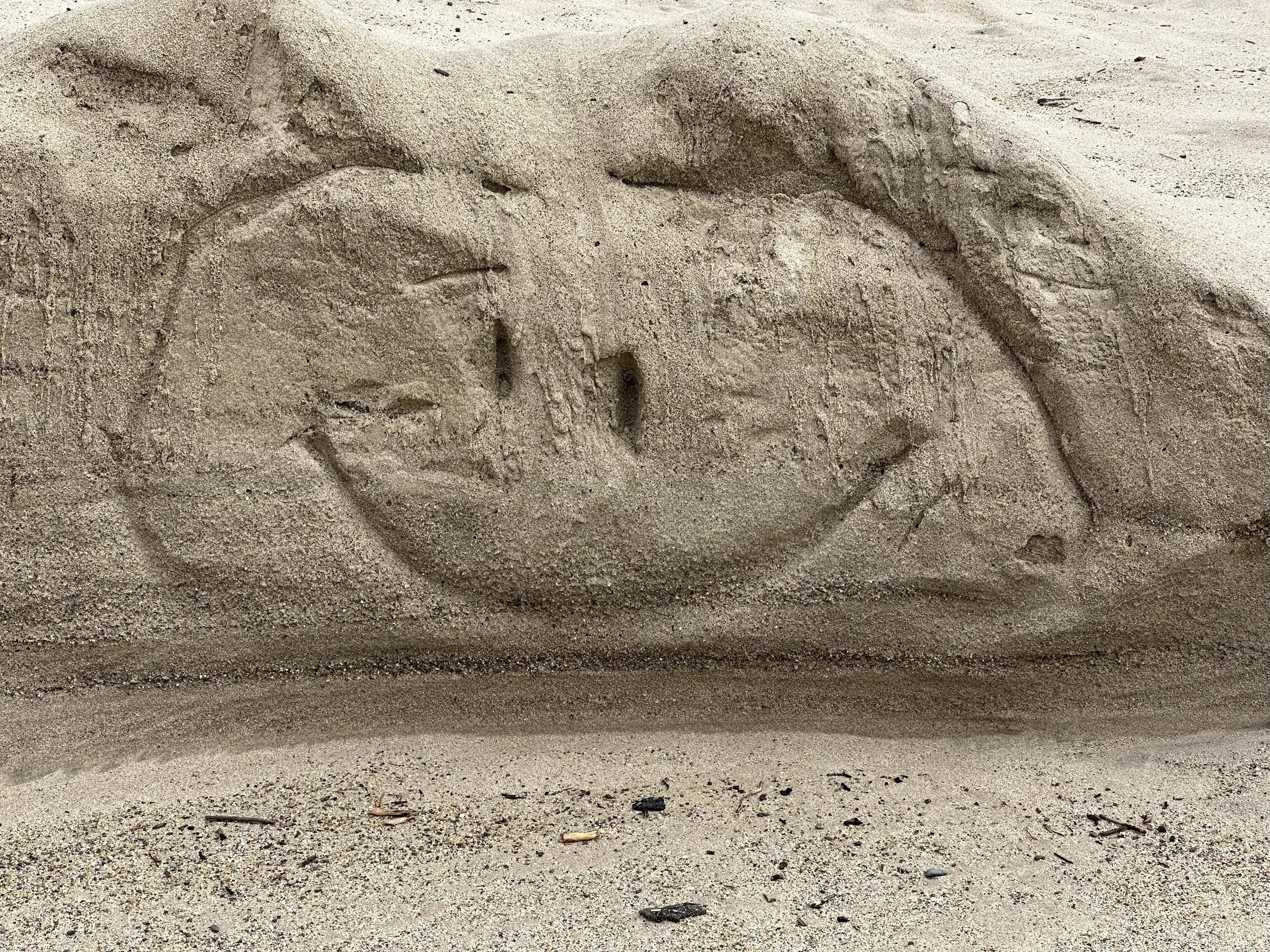 Close-up of a sandy surface with a heart shape drawn in the sand.