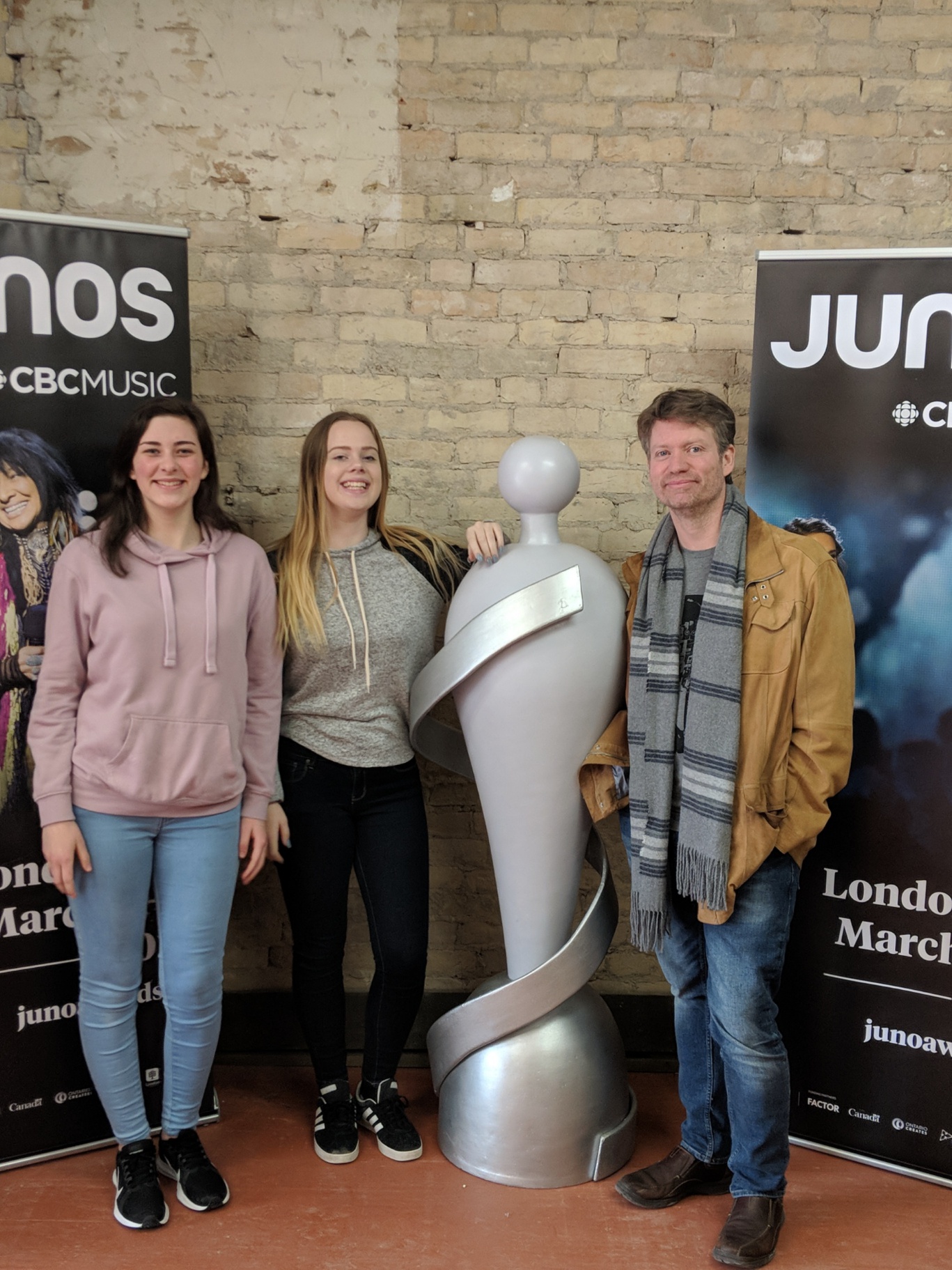 Jenn & Maddie stand in front of Budweiser Gardens in London, where the JUNO Awards will be held on Sunday, March 17th. Second photo: Emily, Jenn & Andrew gather around the life-size JUNO statue that has been added inside JUNO House at 658 Dundas Street in Old East Village in London.