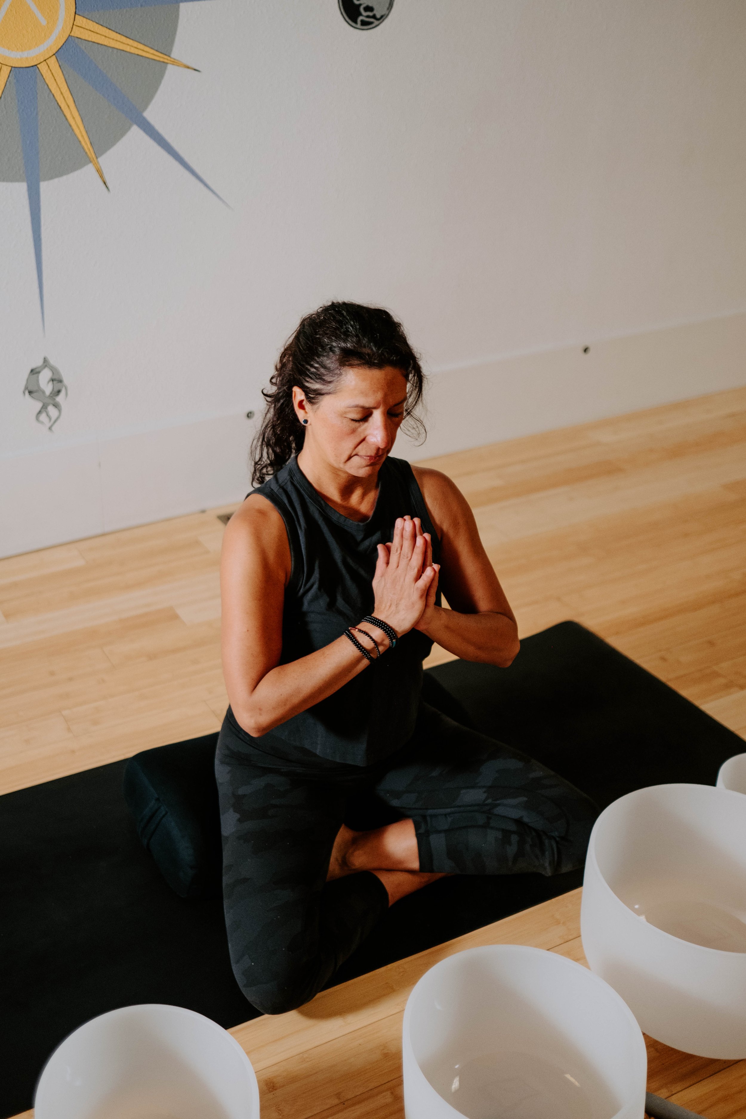 Woman meditating on yoga mat with singing bowls around her