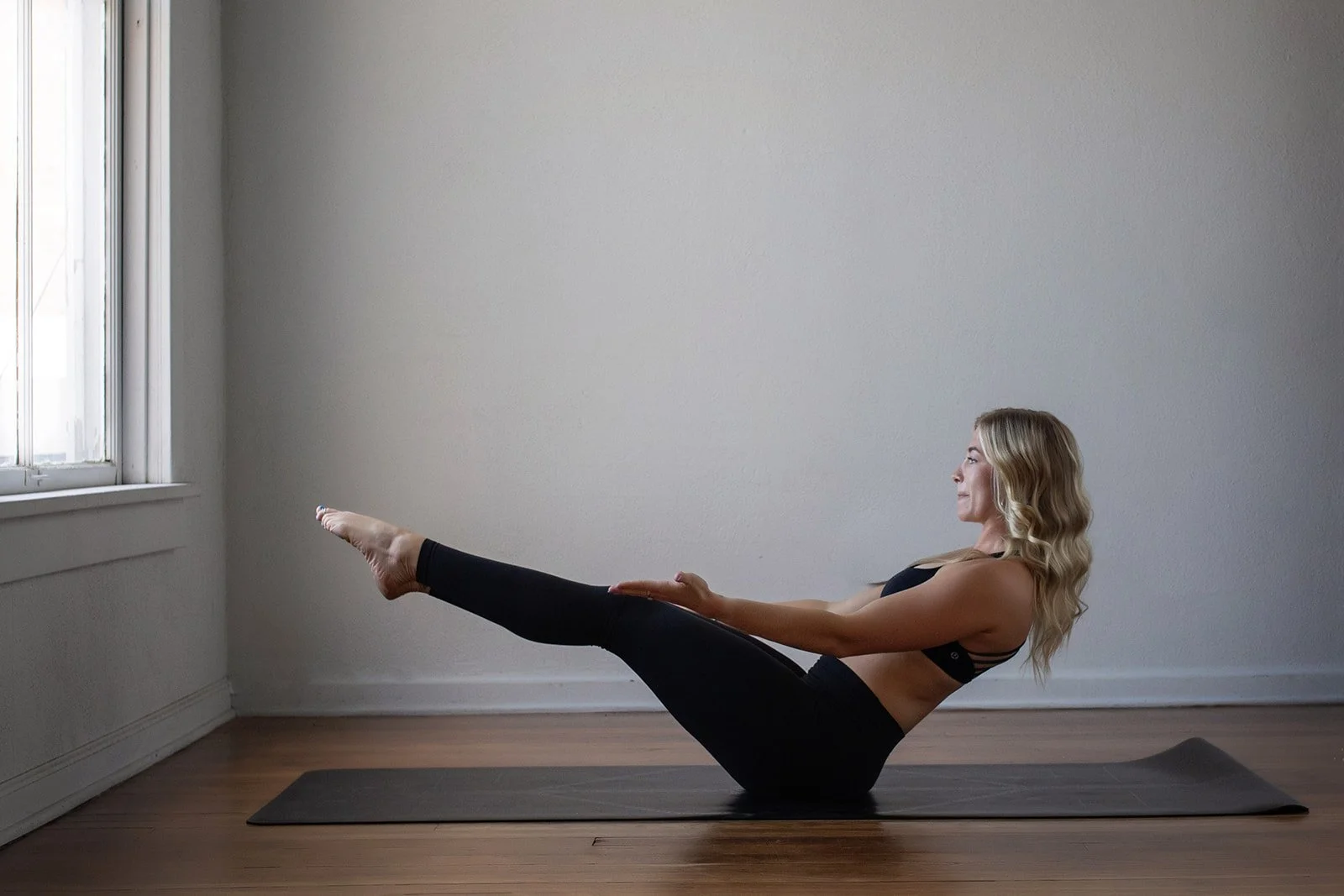 A woman practicing yoga in a plank position on a black mat in front of a white brick wall and a door with glass panes.