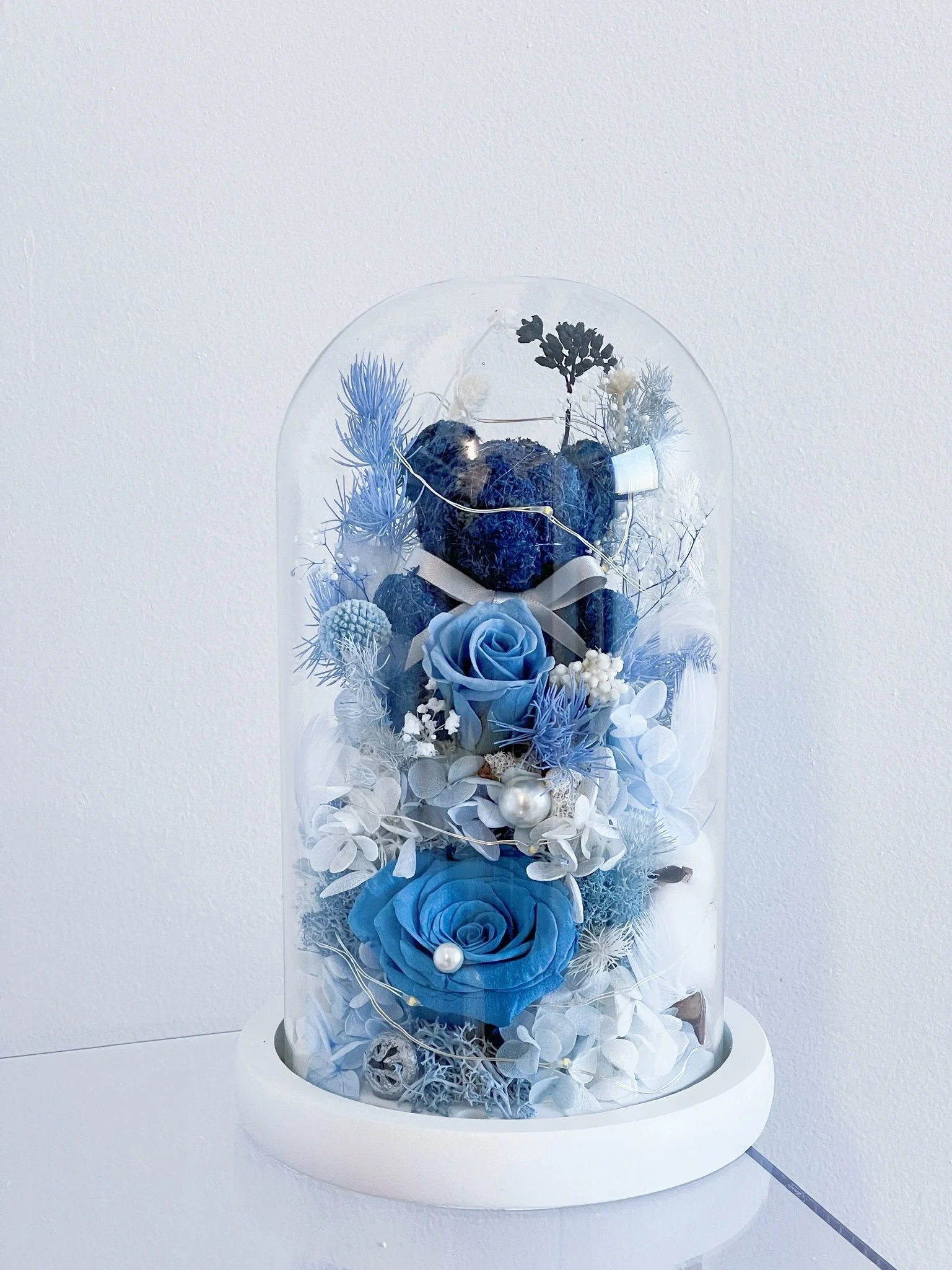 Preserved fresh flowers in tall glass dome with ornaments
