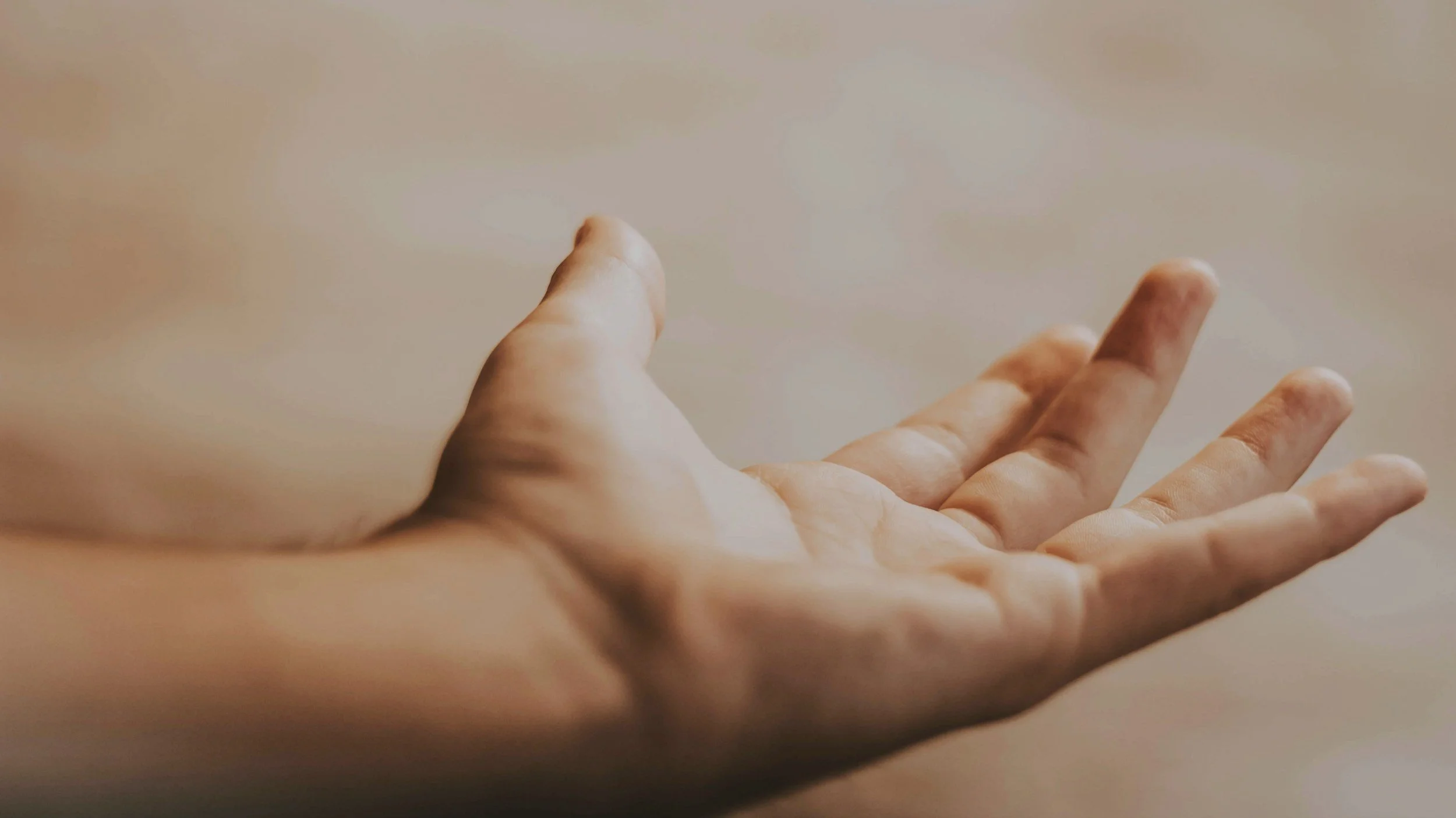 Close-up of an open hand with the palm facing upward, fingers slightly spread, against a blurred neutral background.