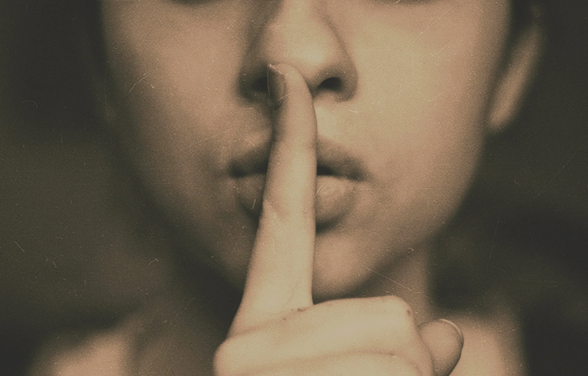 Close-up of a person with a finger pressed against lips in a shushing gesture.