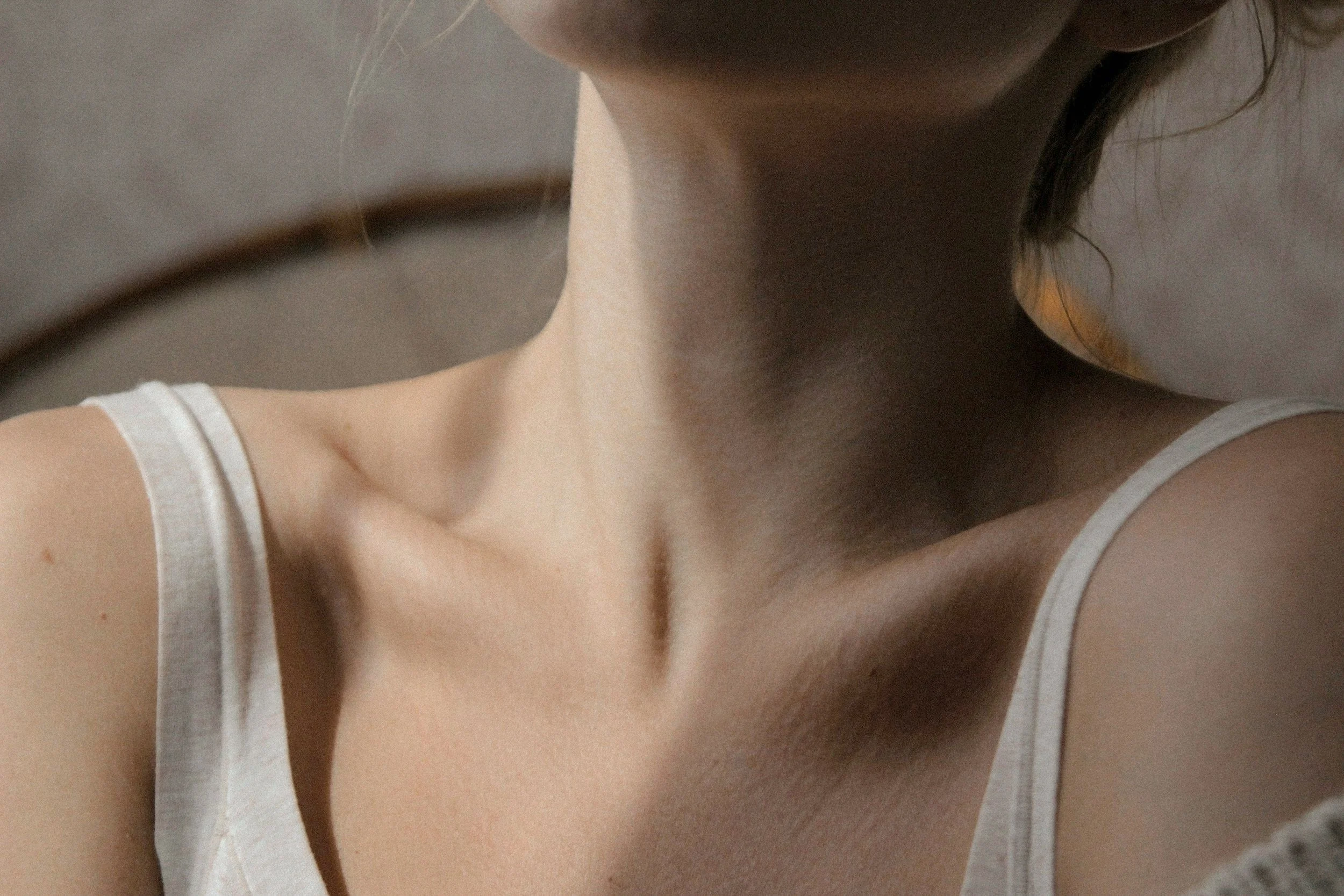 Close-up of a woman's collarbone and shoulder with a white sleeveless top.