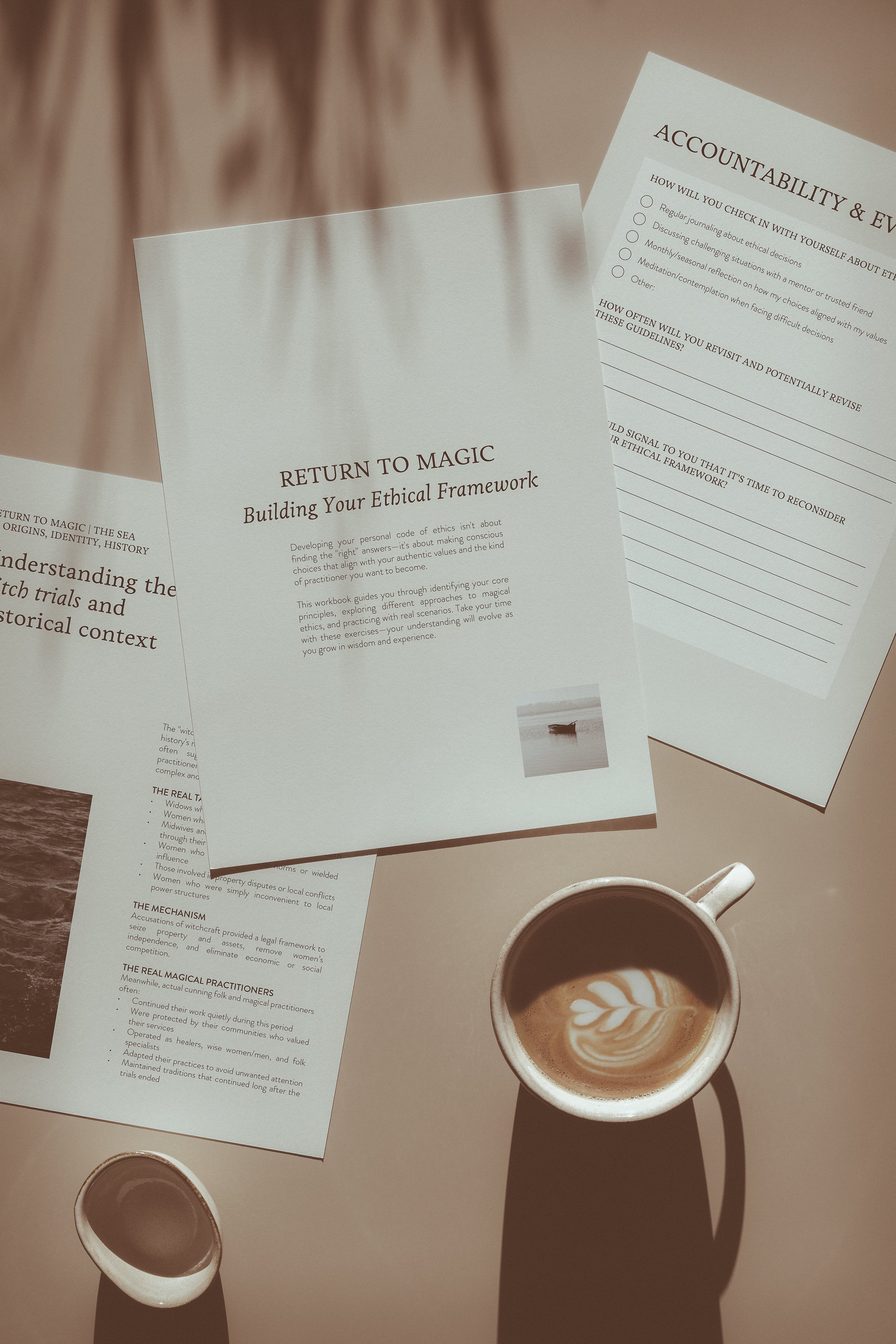 3 workbook pages on a table with a cup of coffee. One reads "Return to Magic: Building Your Ethical Framework." Another is a worksheet for considering your framework. And last, a page that says "understanding the witch trials and historical context."