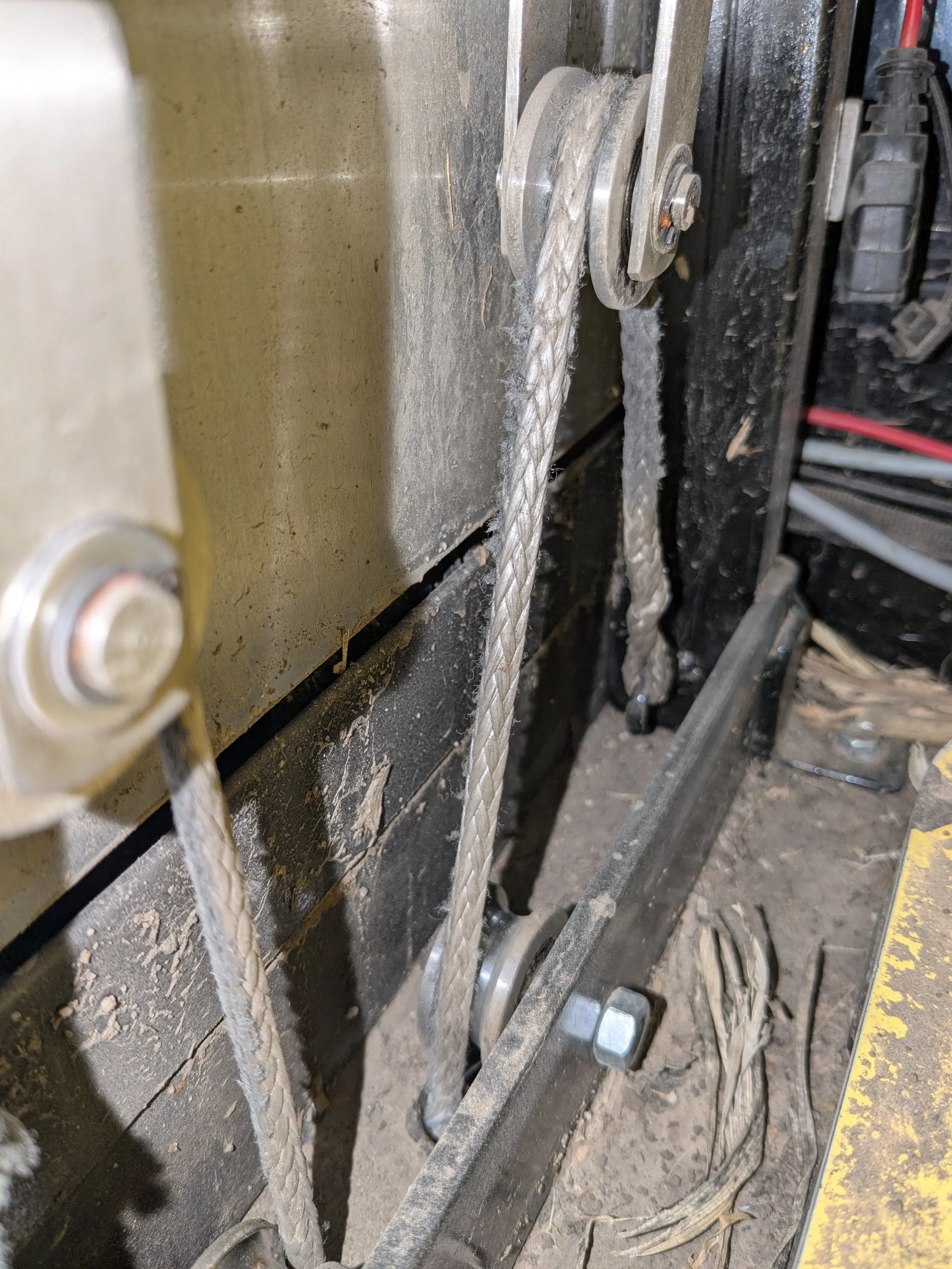 Close-up of a mechanical setup showing two metal pulleys with a braided steel cable running over them, attached to a black and yellow frame.