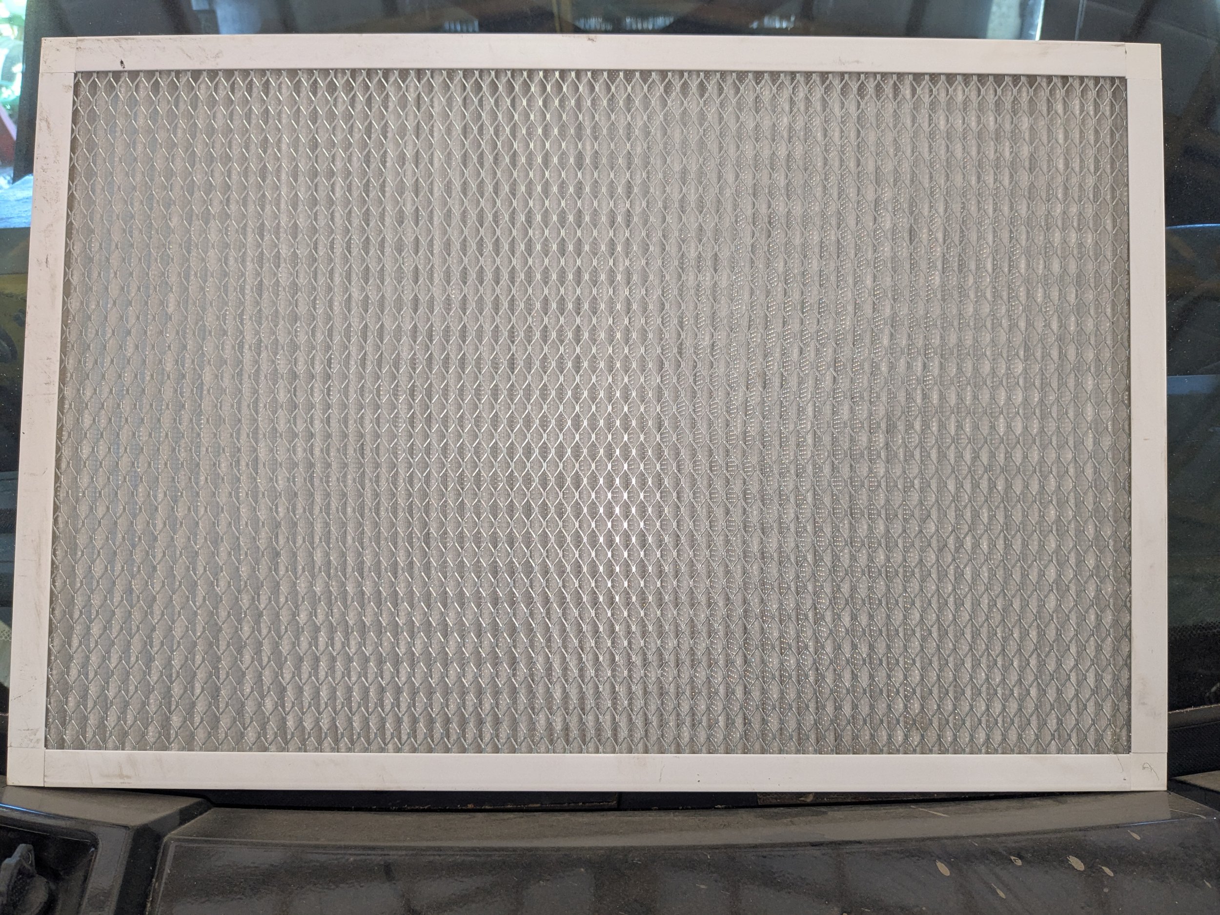 A rectangular air filter with a white metal frame and a honeycomb pattern filtering surface.