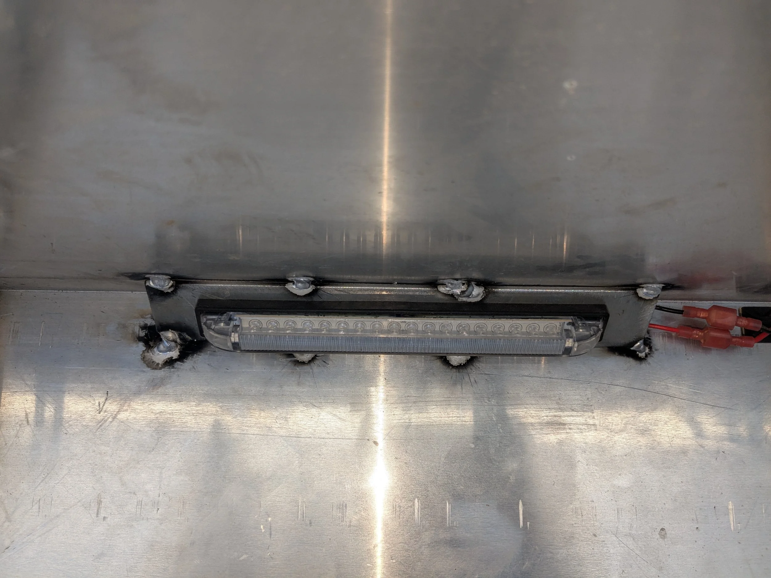 LED light bar mounted on a metallic surface with visible screws and wires.