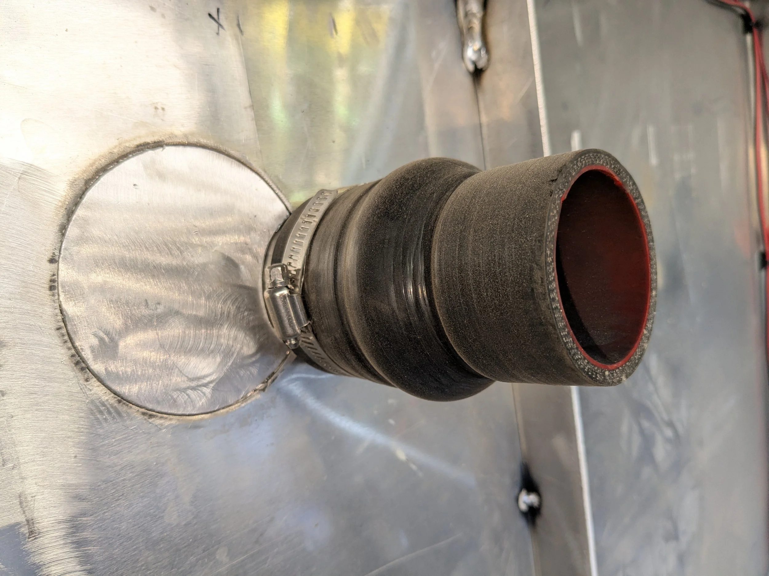 Close-up of turbocharged engine intake pipe connected to a metal flange with a pipe clamp in a workshop setting.