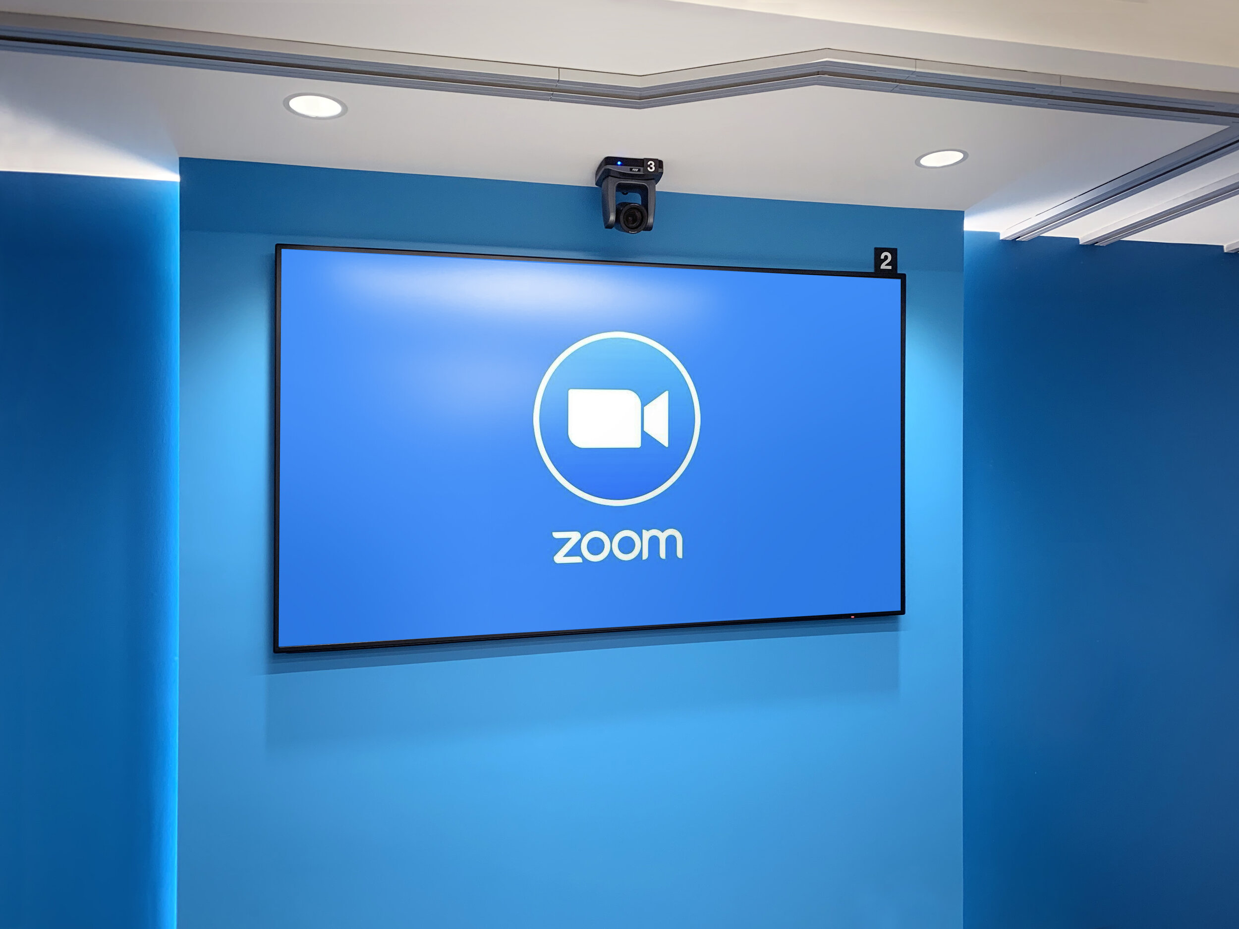  A 65-inch screen presents a Zoom splash screen, ready for a video conference to be started. The TVs are numbered to allow a guest to identify and control them via the wall-mounted touchscreen control. 