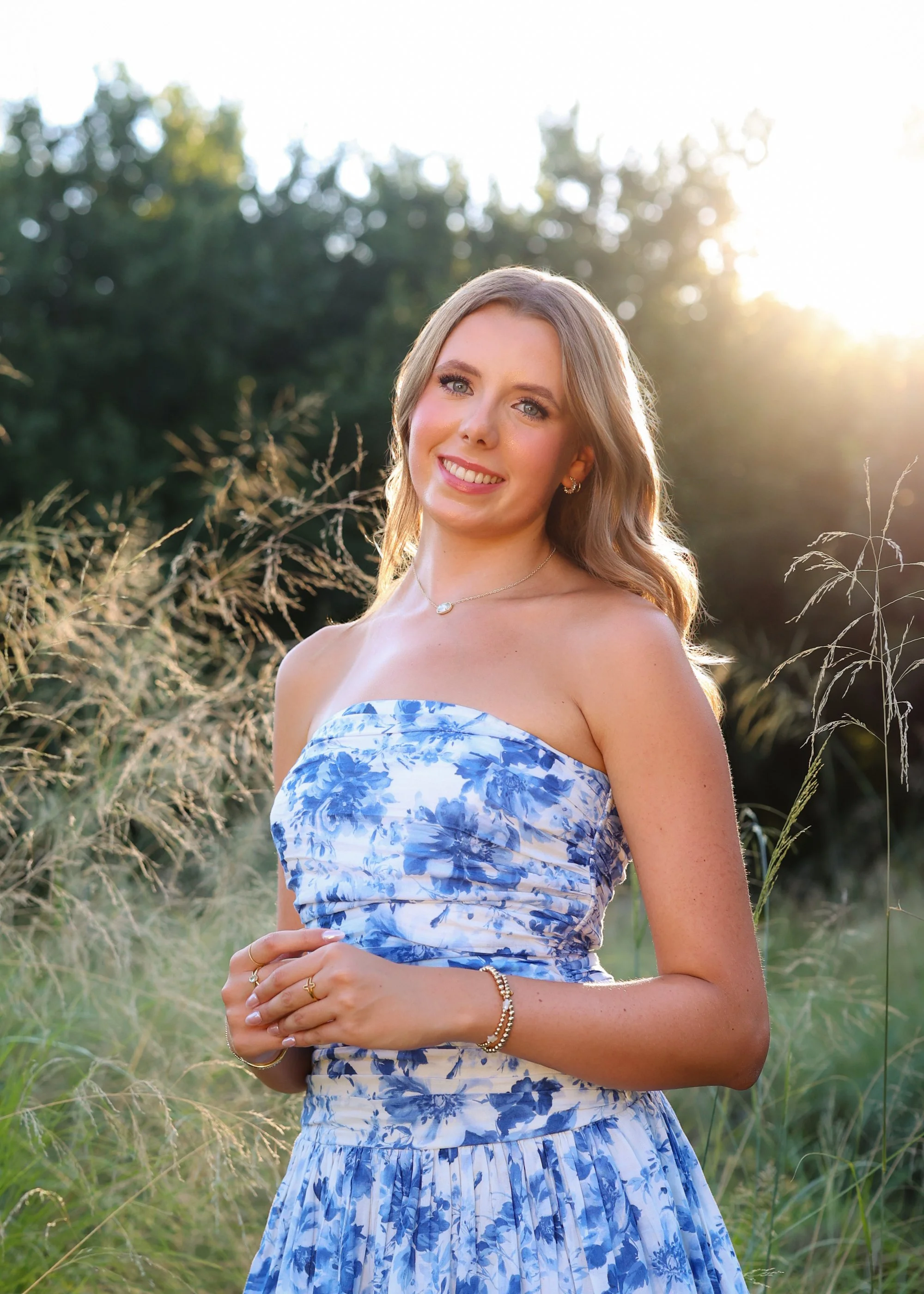 a smiling high school senior wearing a strapless blue floral dress in tall grasses in Raleigh