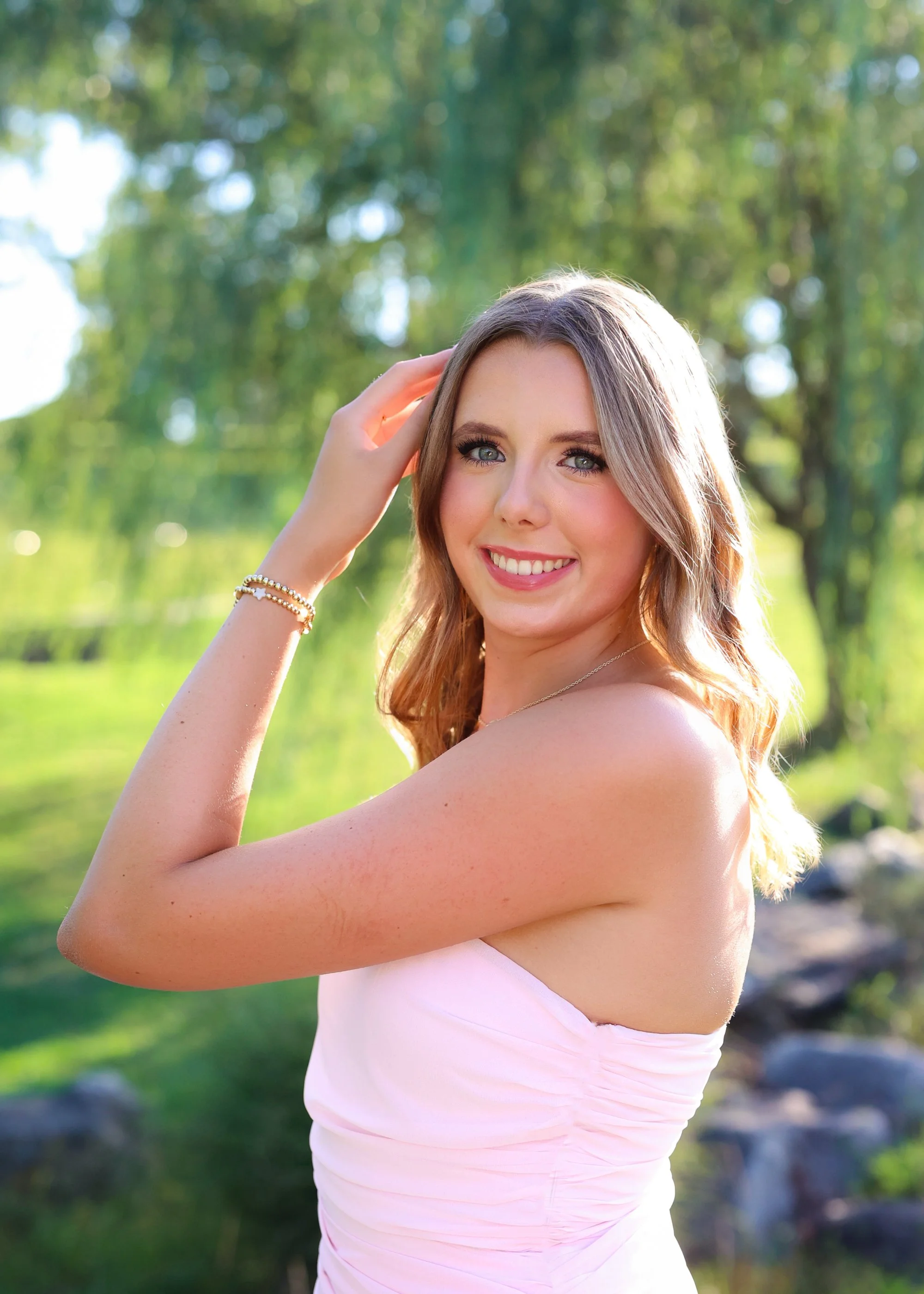 a class of 2027 senior female wearing a pink dress and smiling and sun is reflecting off her hair in Raleigh