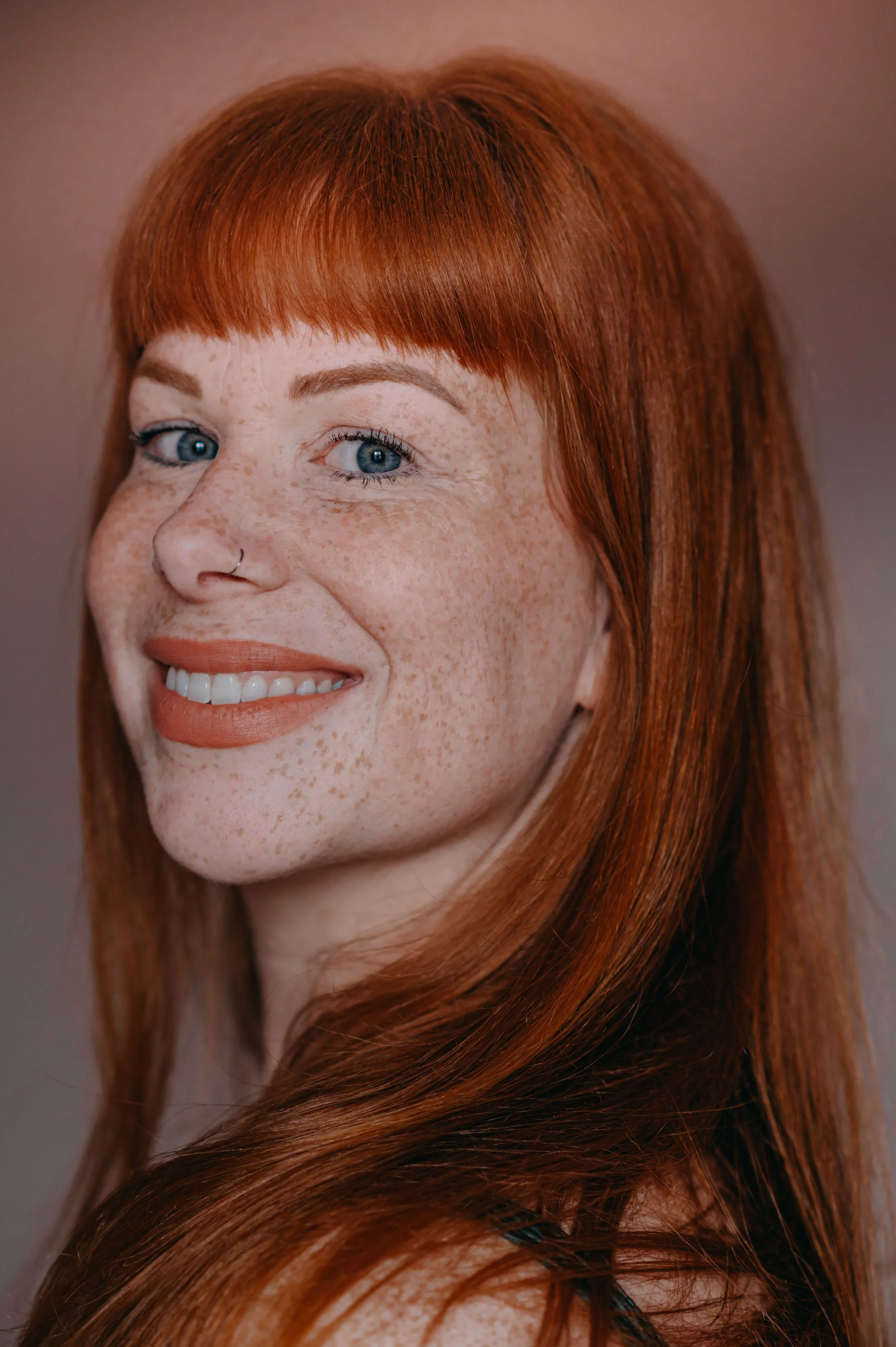 Close-up of a woman with red hair and freckles, smiling and looking at the camera.