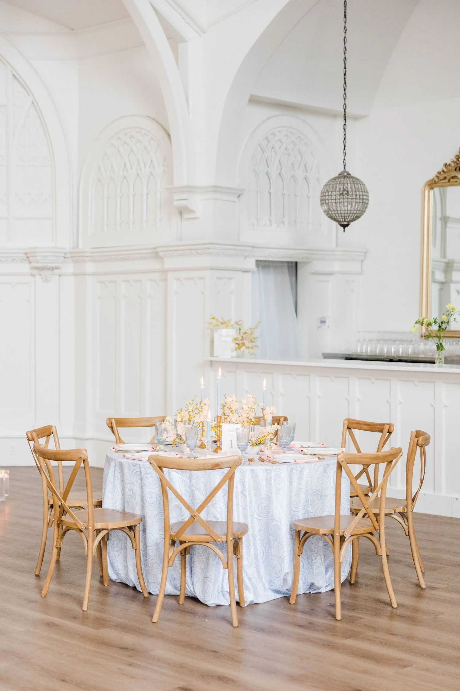 White interior of The Broadway Avenue with Gothic tracery windows, a gold mirror, and a reception table set with candles and soft florals