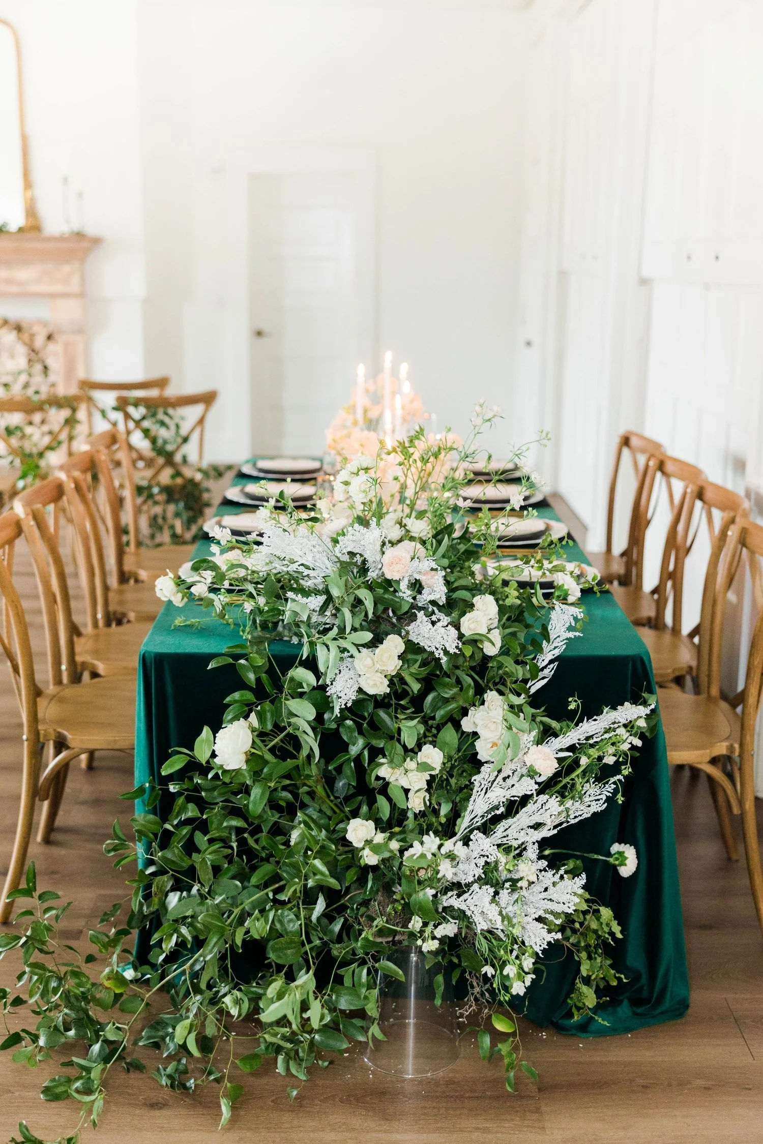 Long reception table with an emerald green tablecloth and an overflowing white and greenery centerpiece, at The Broadway Avenue