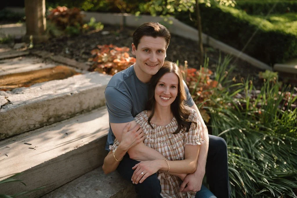 Couple sitting close together on stone garden steps surrounded by greenery, a sweet option for golden hour engagement photoshoot locations.
