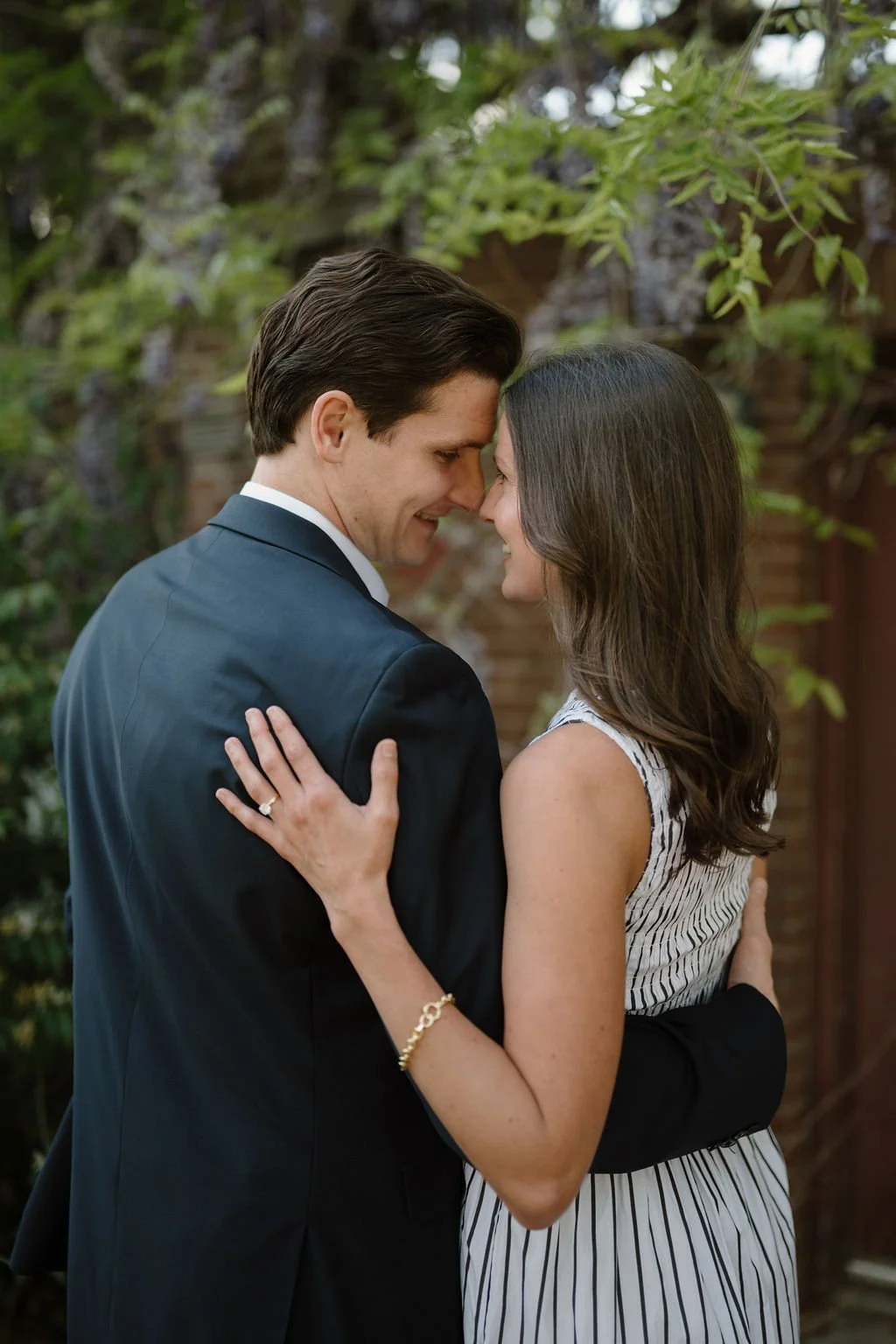 Couple leaning in forehead to forehead with her ring hand resting on his navy suit jacket.