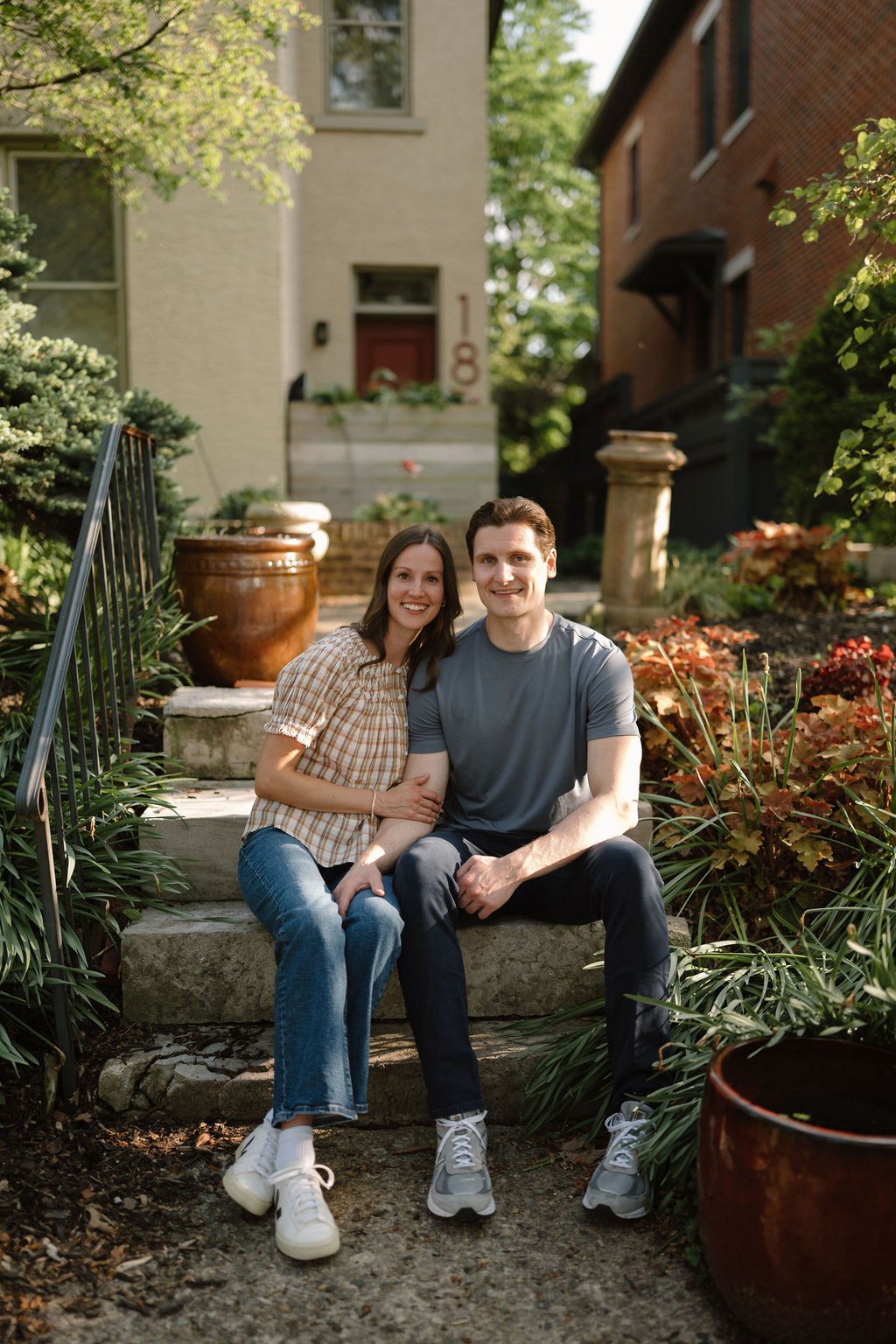 Couple sitting side by side on garden steps in front of a cozy home, a relaxed and personal take on at-home engagement photoshoot locations.