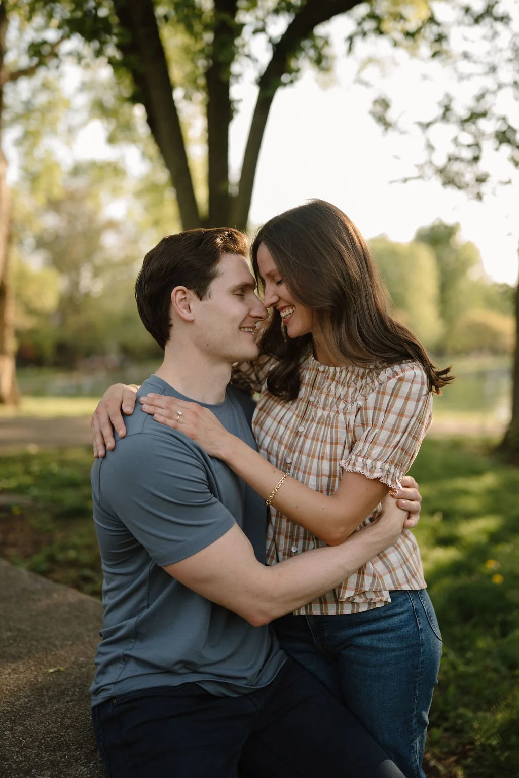 Couple sitting close and laughing nose to nose in warm evening light by a park pond.