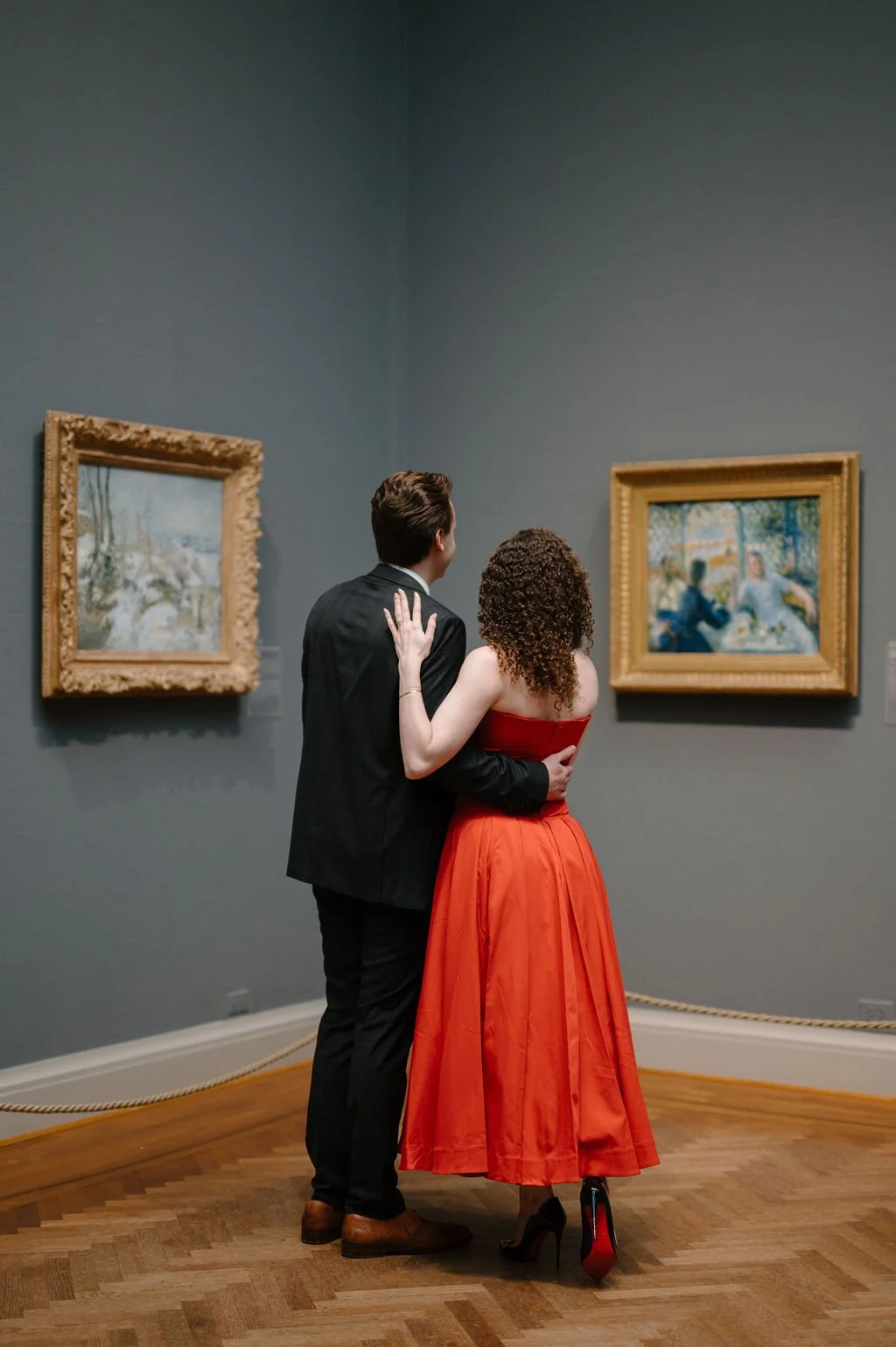 Couple standing arm in arm, seen from behind, looking at Impressionist paintings in a museum gallery