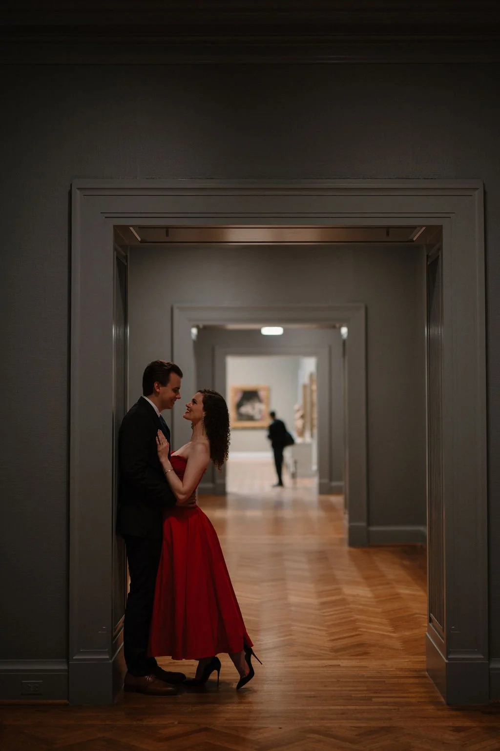Couple embracing in a museum doorway with a herringbone floor and a long gallery corridor behind them