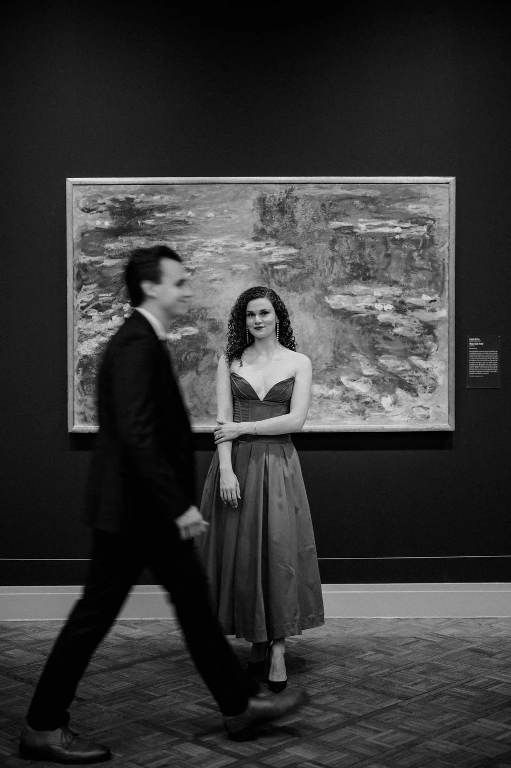 Black and white Chicago engagement photos of a woman posing before a Monet painting as her fiancé walks past in motion blur
