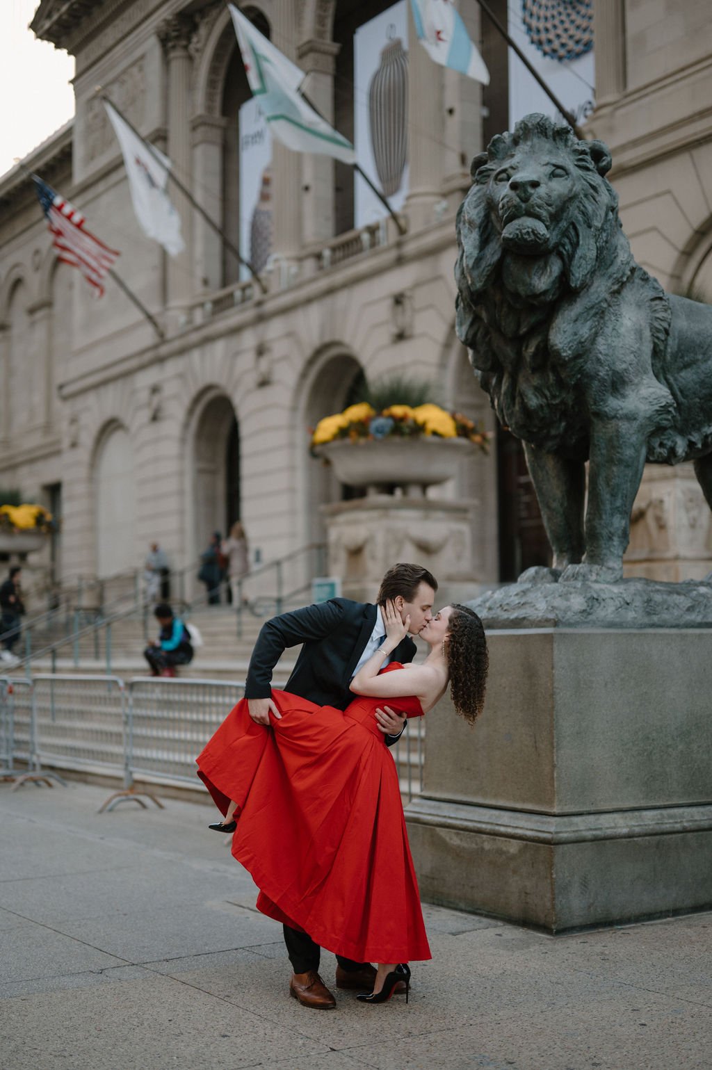 Couple in a dramatic dipped kiss beside the bronze lion at the Art Institute of Chicago, she in a flowing red dress