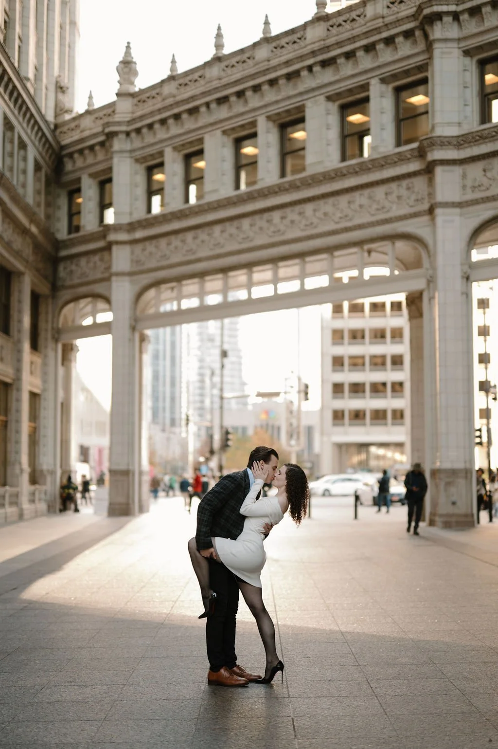 Chicago engagement photos of a couple sharing a dipped kiss beneath the ornate Wrigley Building archway in golden light