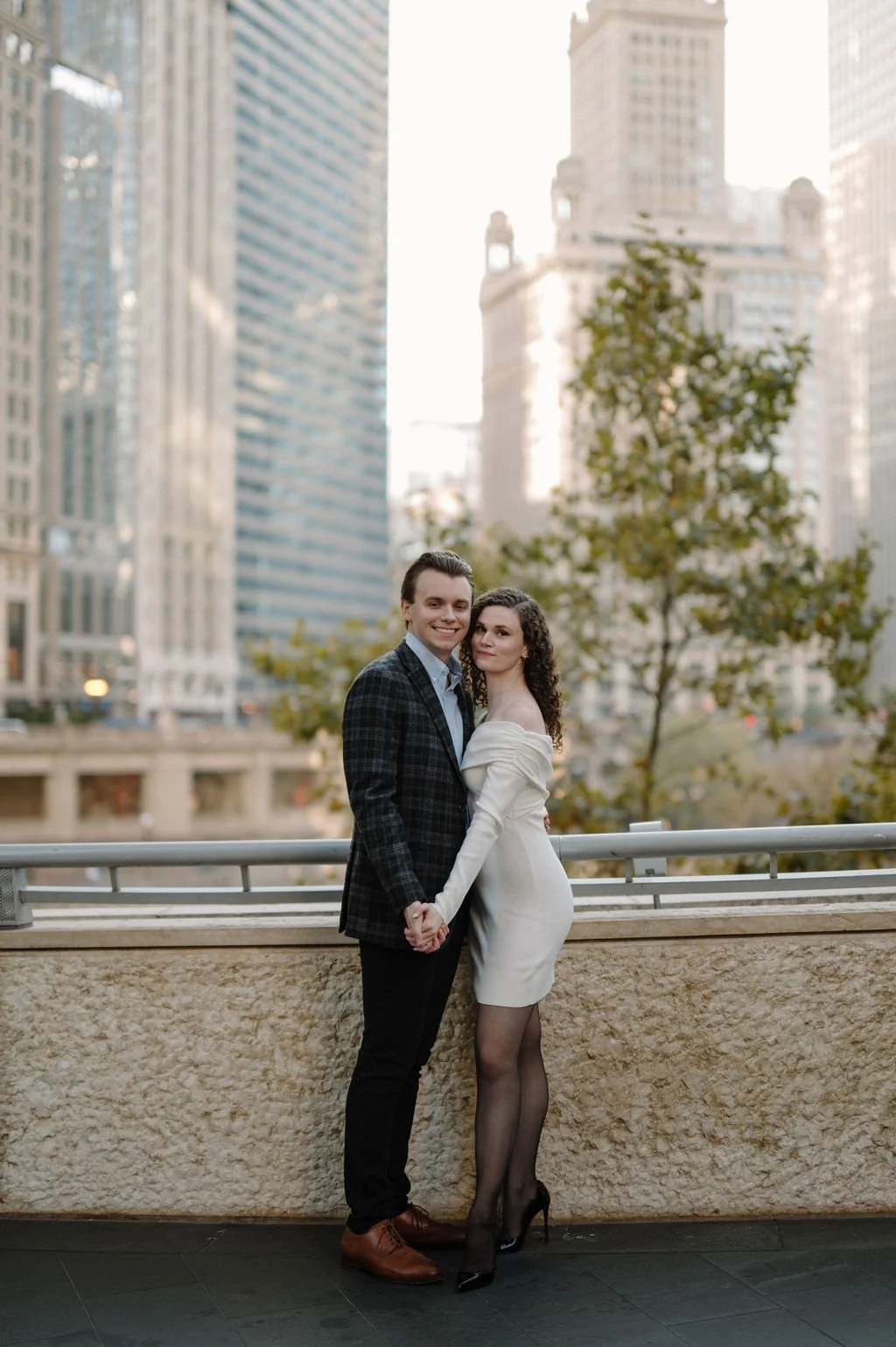 Chicago engagement photos of a couple posing hand in hand on a downtown Chicago overlook, she in a white dress