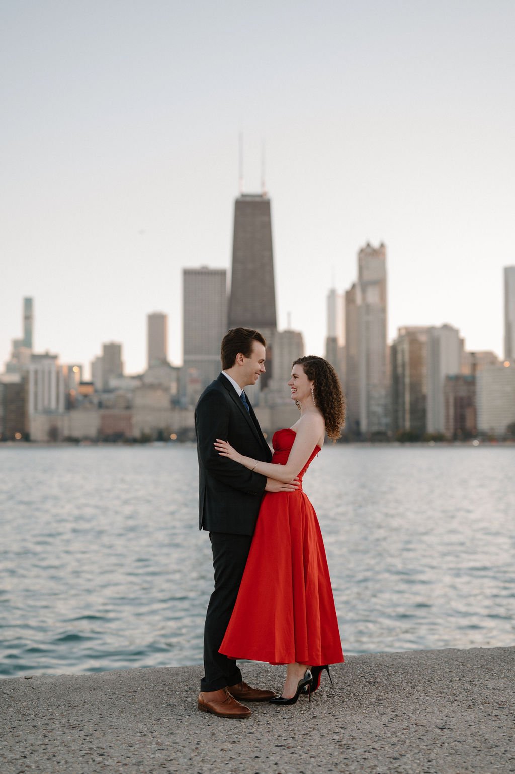 Chicago engagement photos of a smiling couple embracing along Lake Michigan with the skyline behind them