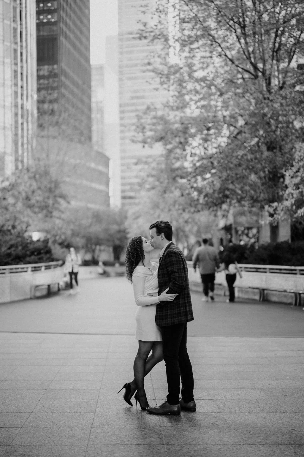 Black and white Chicago engagement photos of a couple kissing on a tree-lined downtown plaza