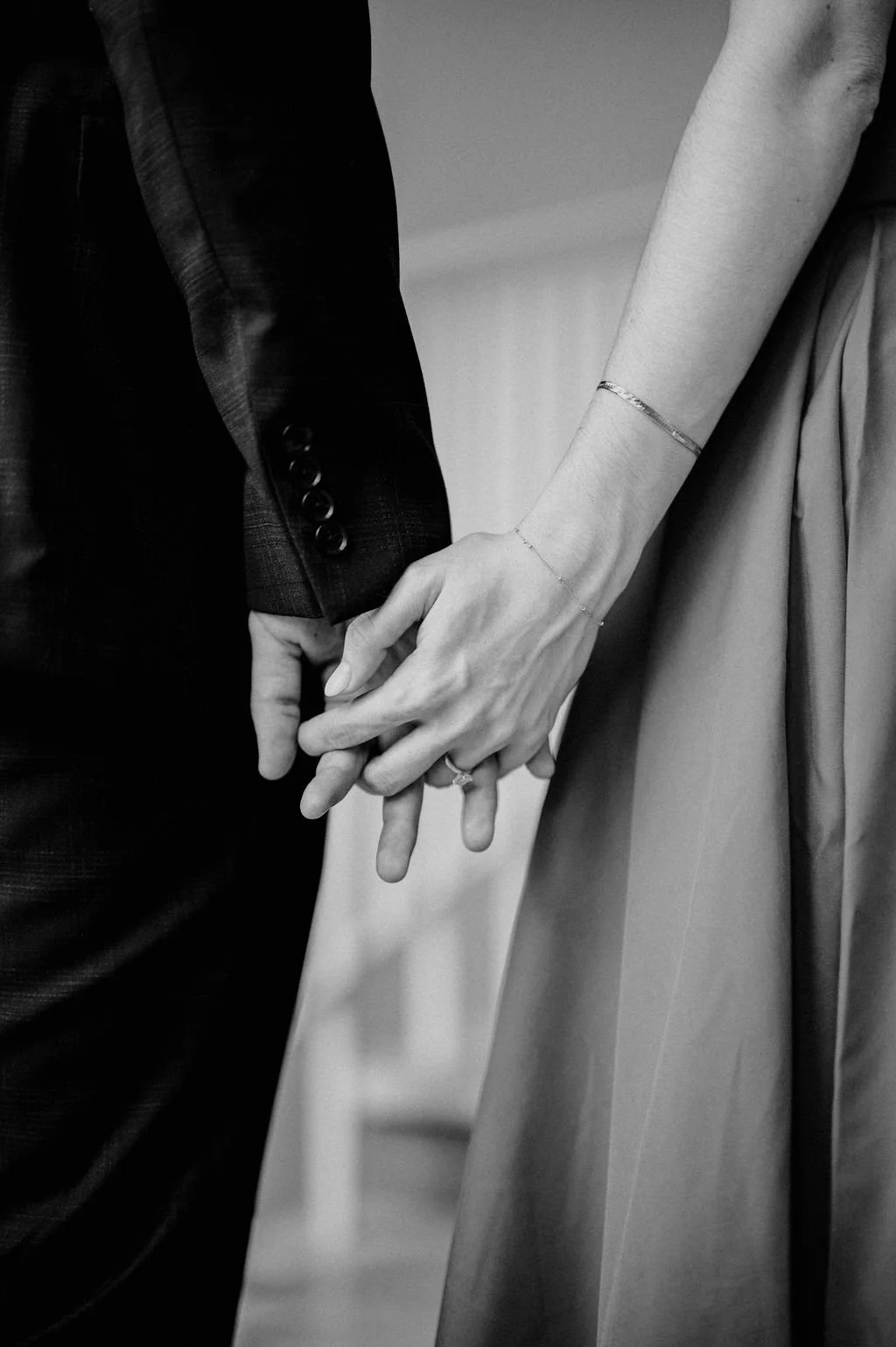 Black and white close-up of a couple holding hands, her engagement ring and delicate bracelets visible