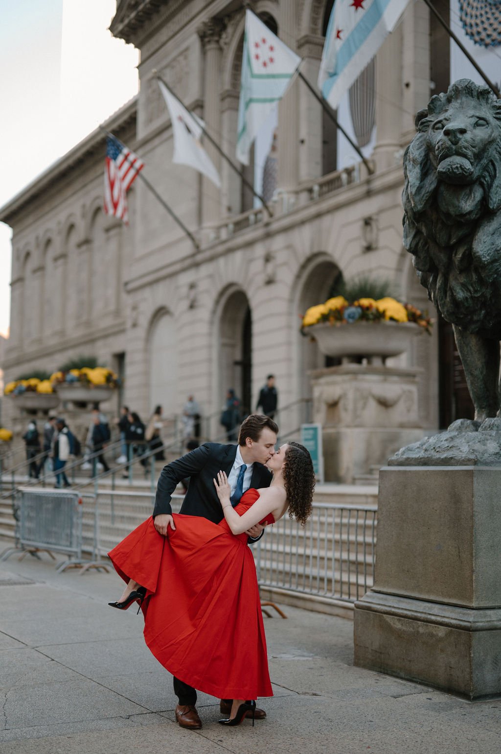 Couple in a dramatic dipped kiss beside the bronze lion at the Art Institute of Chicago, she in a flowing red dress