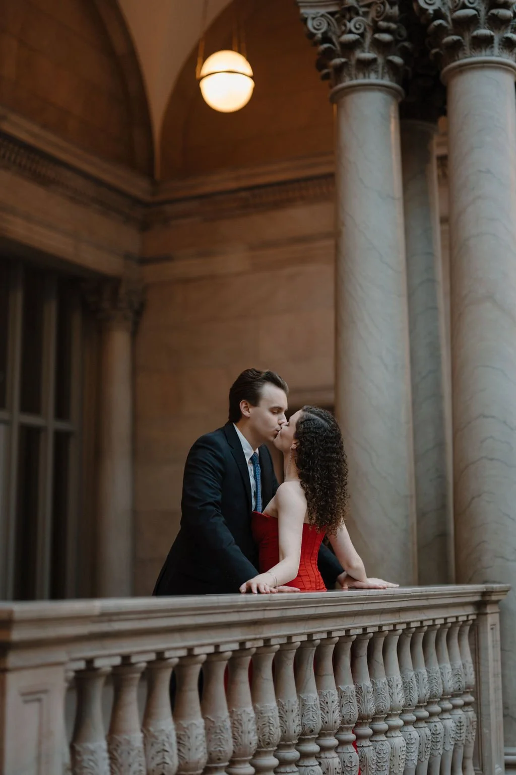 Chicago engagement photos of a couple kissing on a marble balcony at the Art Institute of Chicago, she in a red dress
