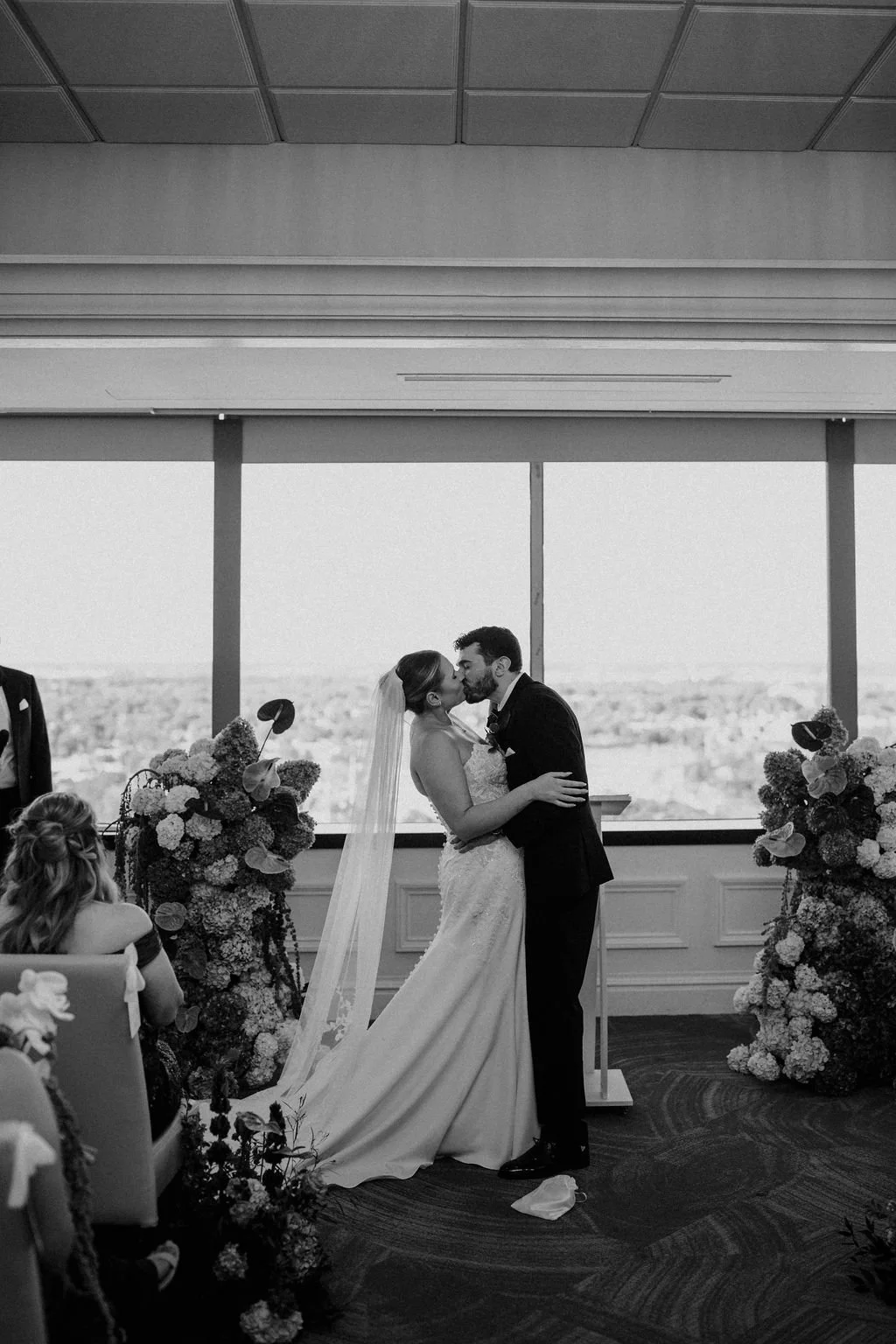 Black and white photo of the couple’s first kiss as husband and wife at the ceremony, with hydrangea and anthurium floral arrangements at one of the most scenic Fort Wayne wedding venues