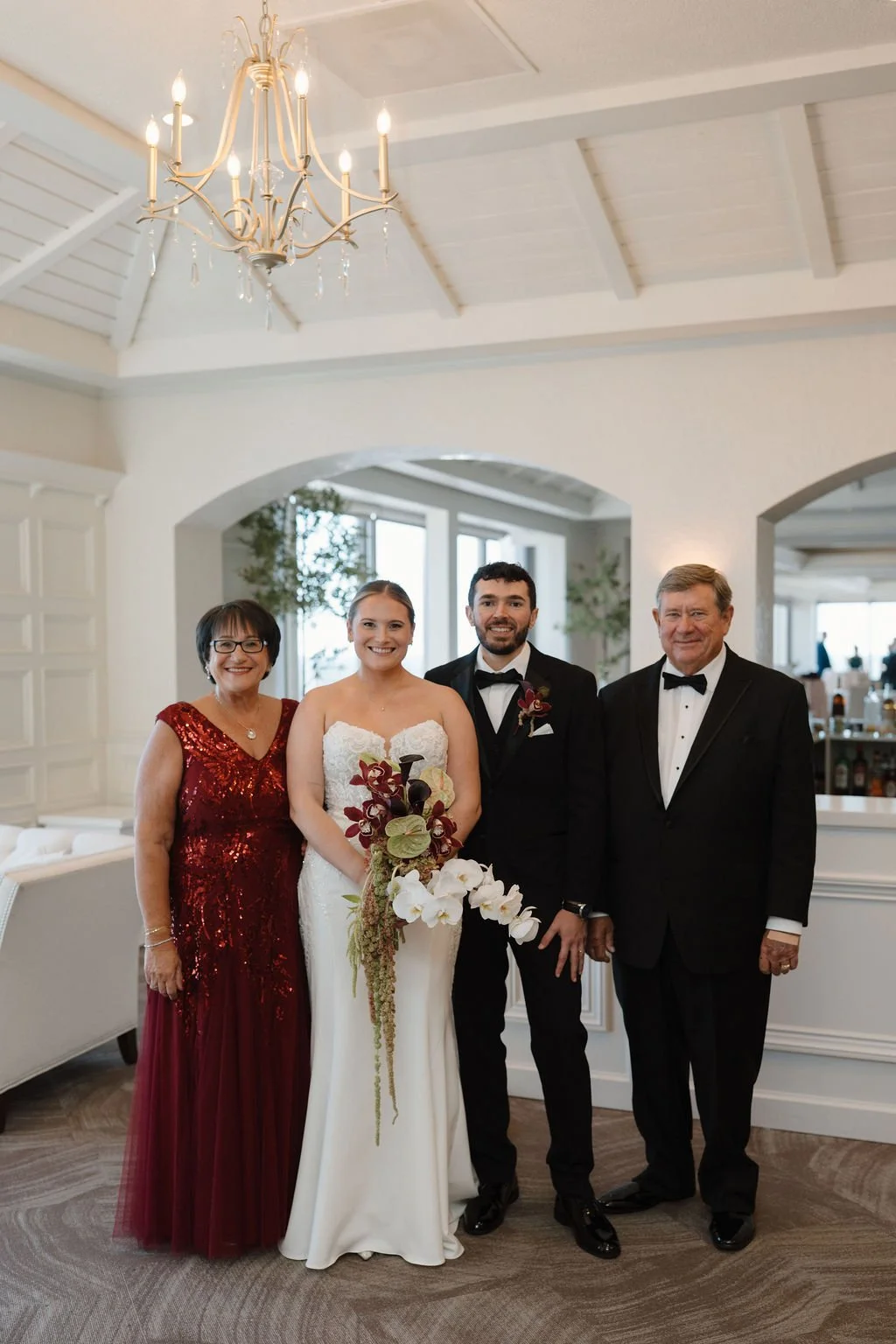 Wedding family portrait of the bride and groom standing under a gold candle chandelier in one of the elegant Fort Wayne wedding venues