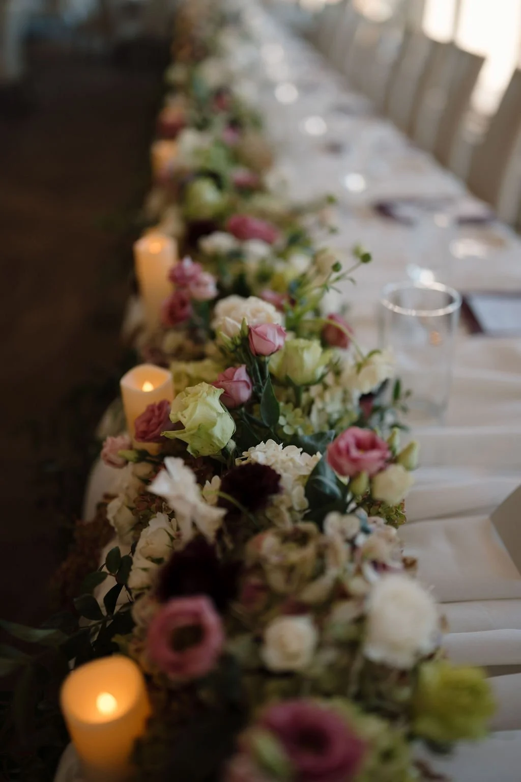 Head table garland of pink, cream, and green blooms with glowing pillar candles, a romantic detail from one of the Fort Wayne wedding venues