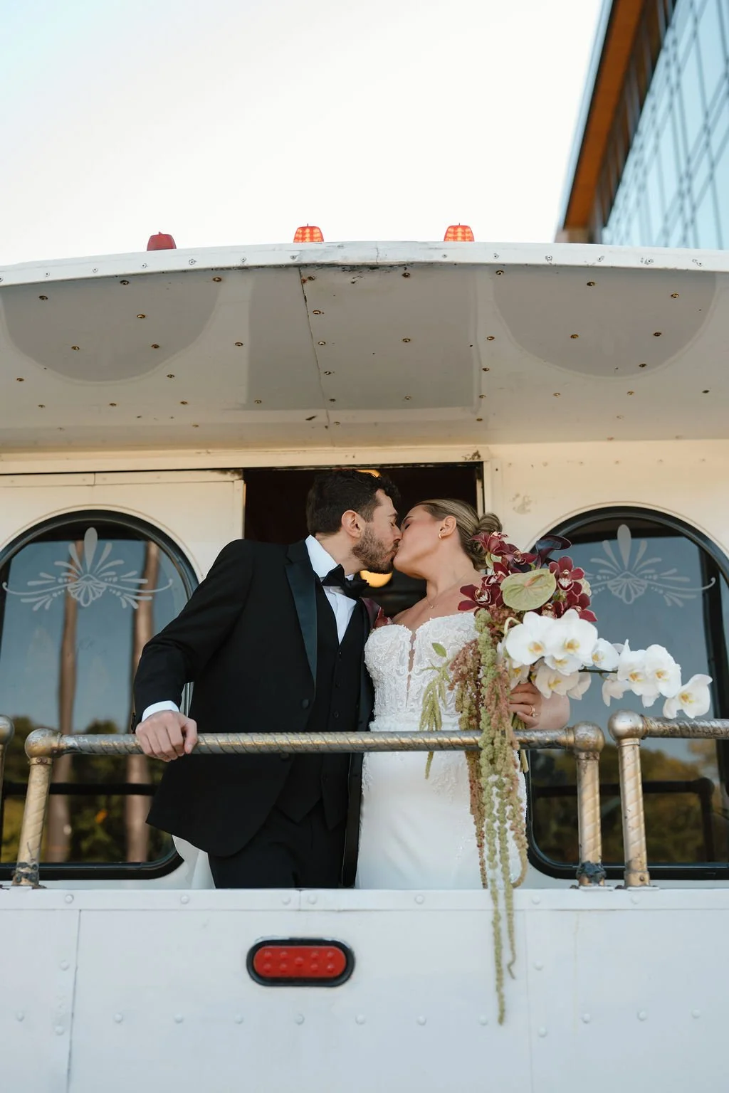 Bride and groom kiss on a white trolley platform with her cascading orchid bouquet, a fun getaway moment from one of the Fort Wayne wedding venues